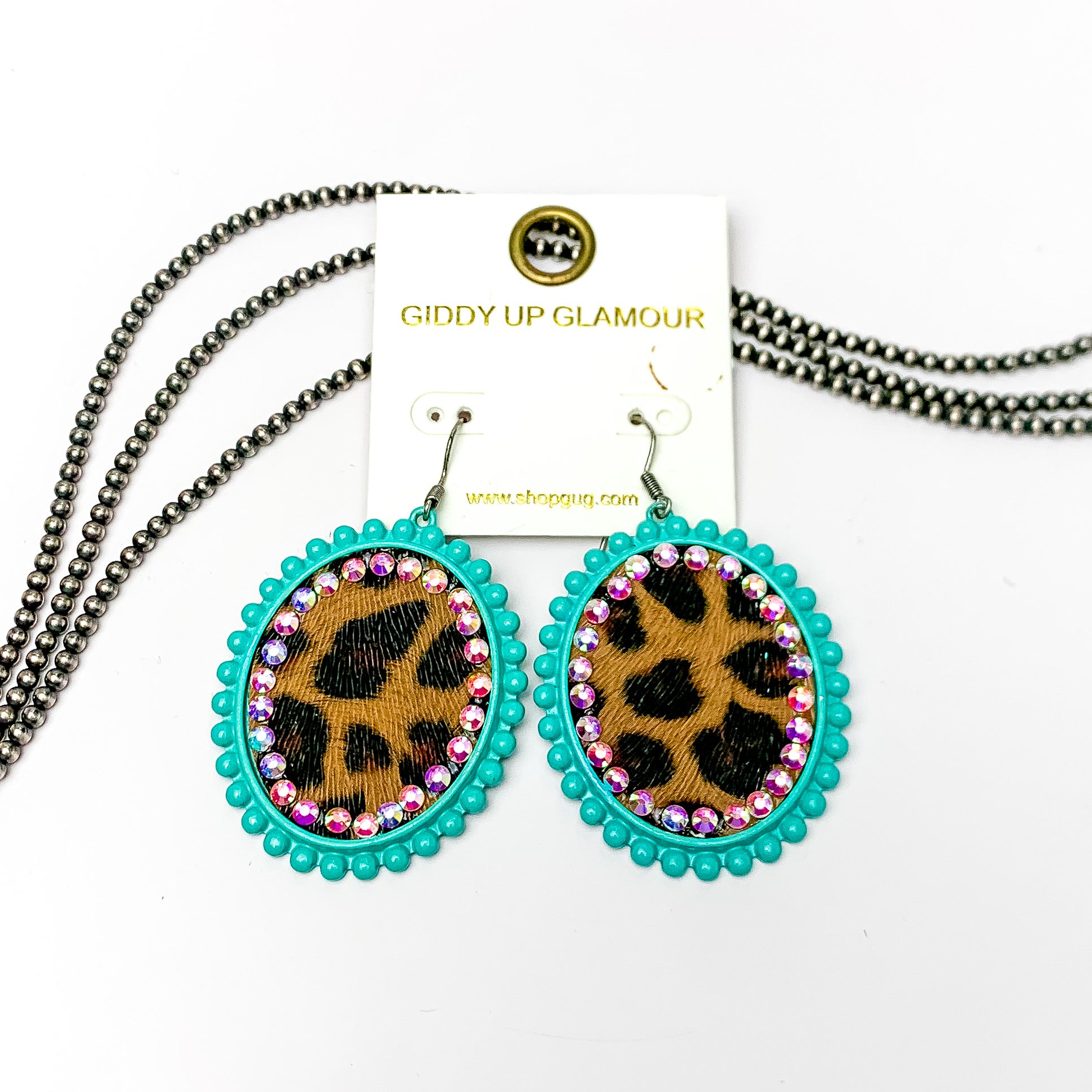 These earrings are oval shaped with leopard print inlay with the outline of the earring is turquoise but also has ab crystal going around the oval shape. These pair of earrings are pictured on a white background with navajo pearls behind it.