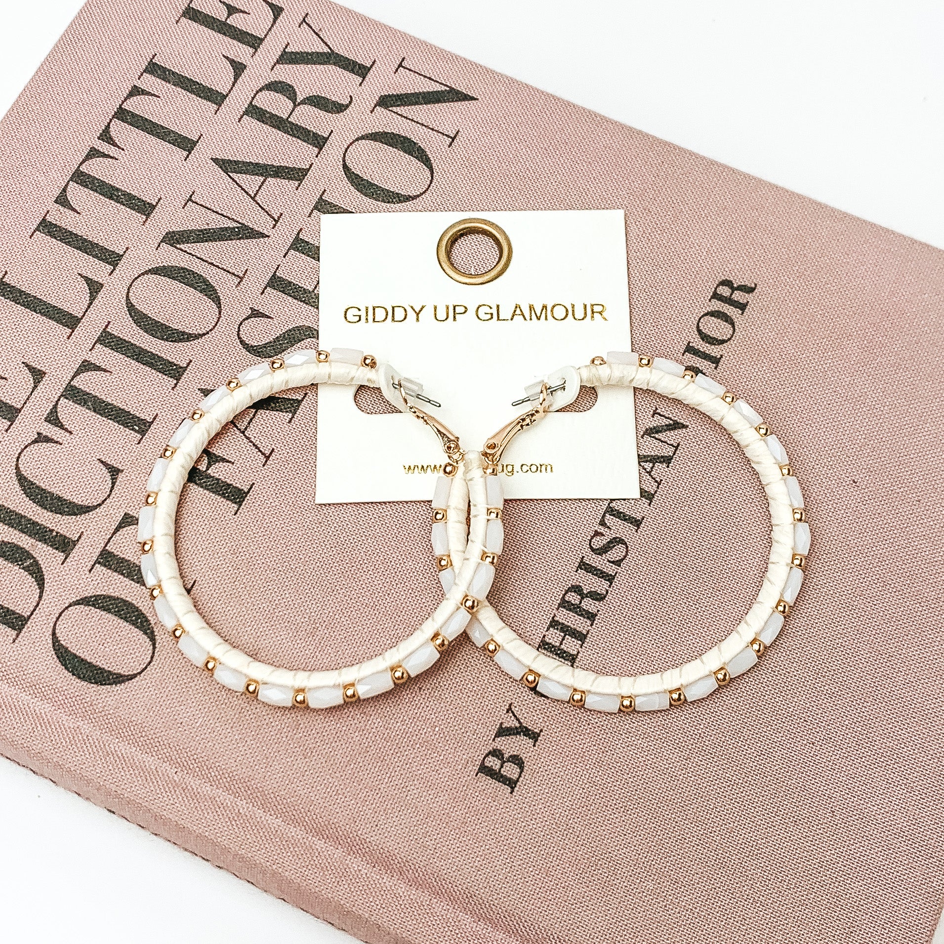 Pictured are circle beaded hoop earrings with gold spacers in ivory. They are pictured with a pink fashion journal on a white background