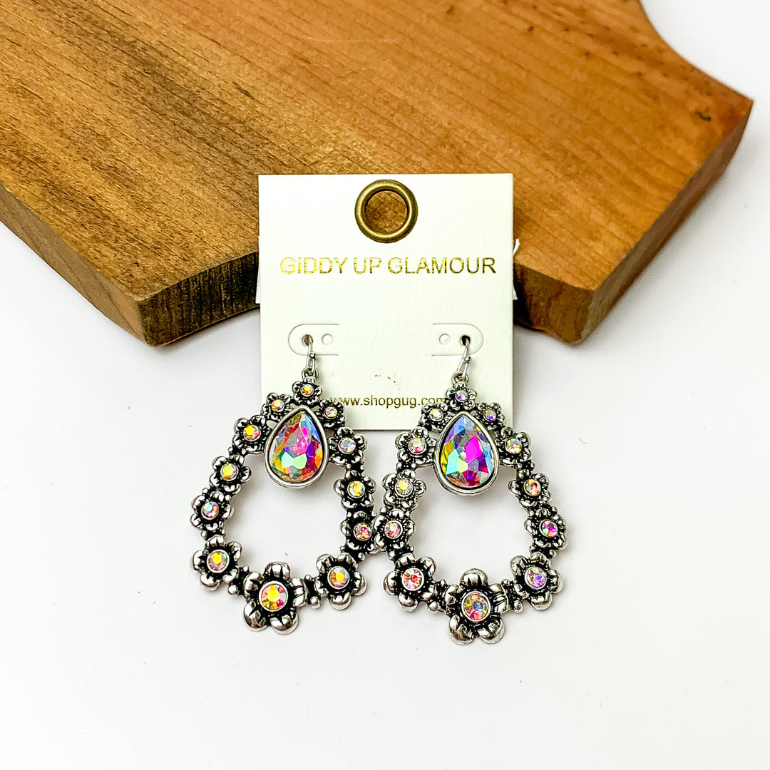 Silver open drop earrings with flowers connecting. Pictured on a white background with a wood piece at the top.