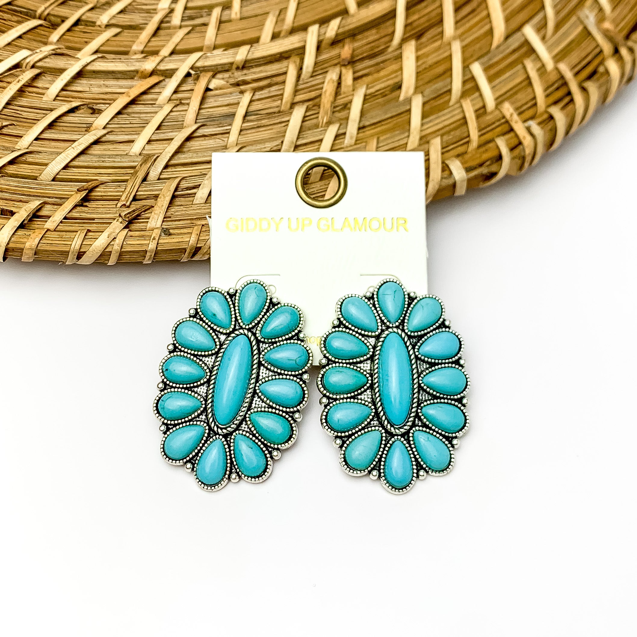 Turquoise and silver tone flower drop earrings. Pictured on a white background with a wood like decoration at the top.