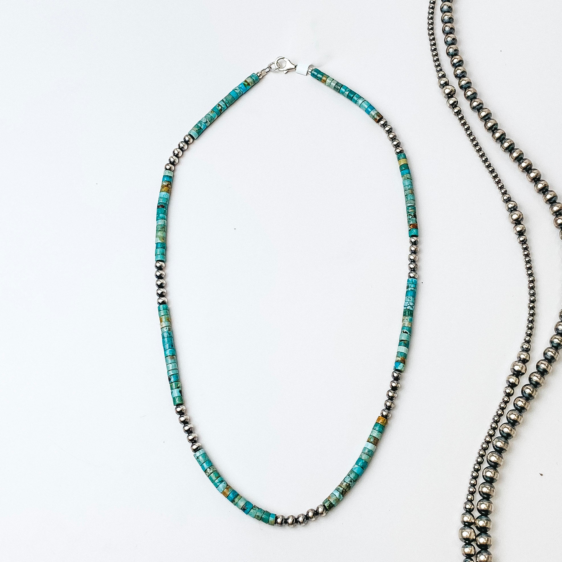 A necklace is centered in the middle of the picture with Navajo pearls laid to the right of the necklace. All on a white background.  