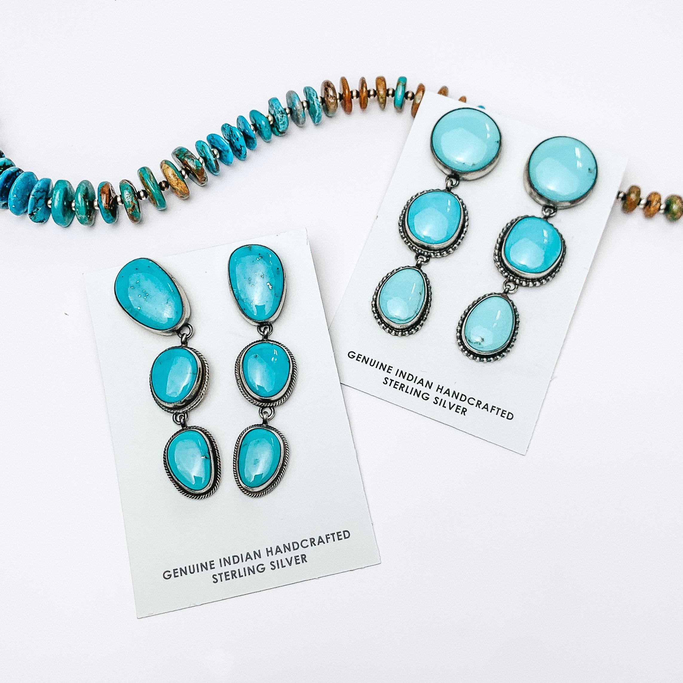 To the left of the picture is stud drop earrings with three turquoise stones. A similar pair is to the right. Above them is a turquoise necklace, all on a white background. 