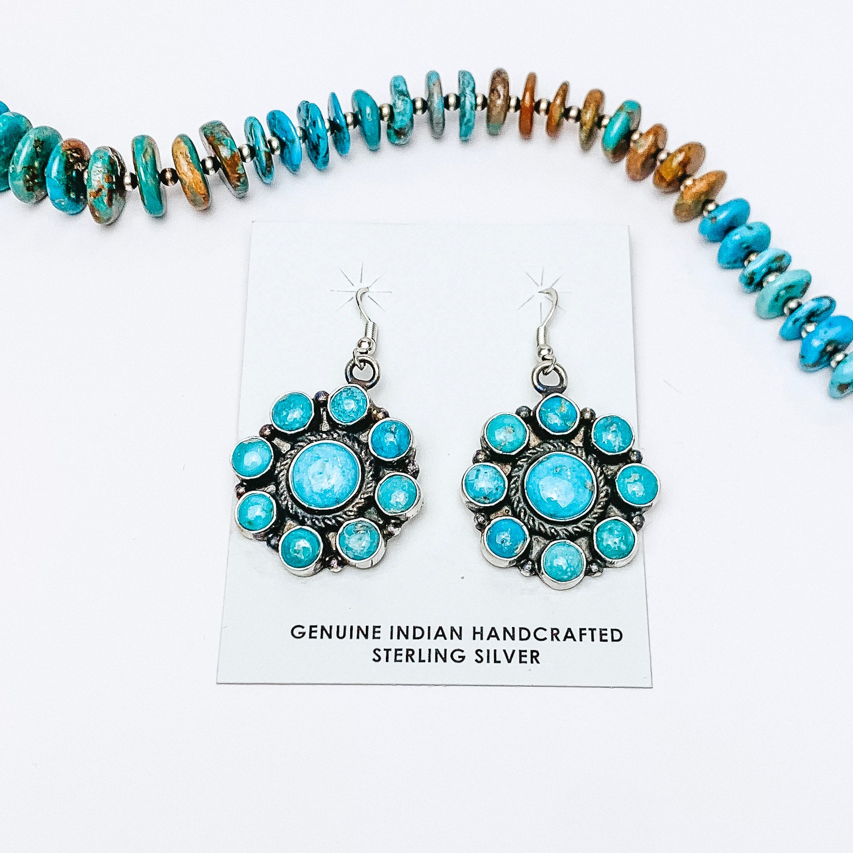 Centered in the middle of the picture is turquoise drop earrings. Above the earrings is a turquoise necklace, all on a white background. 