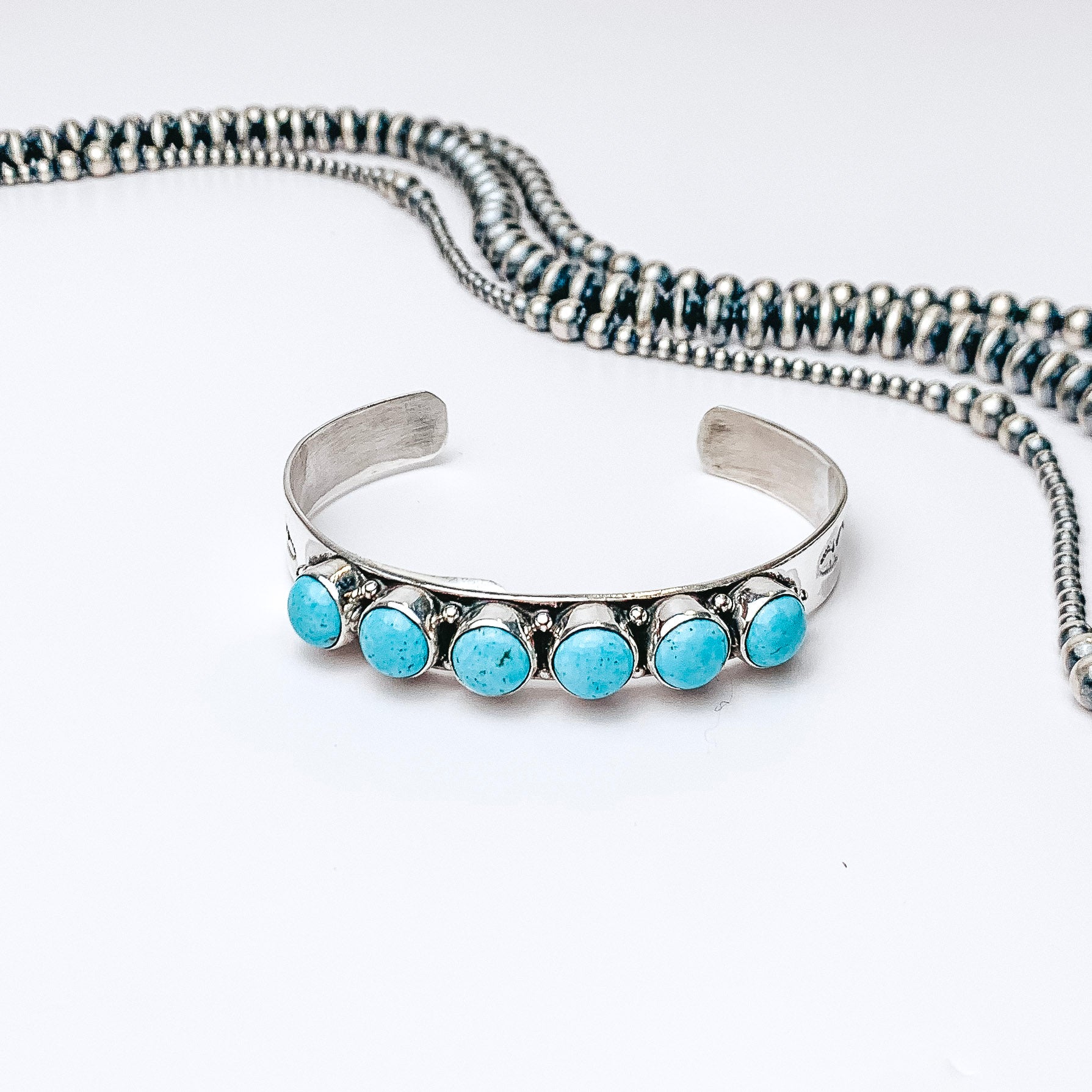 Centered in the picture is a cuff with six kingman turquoise stones. Navajo pearls are laid above the cuff, all on a white background.
