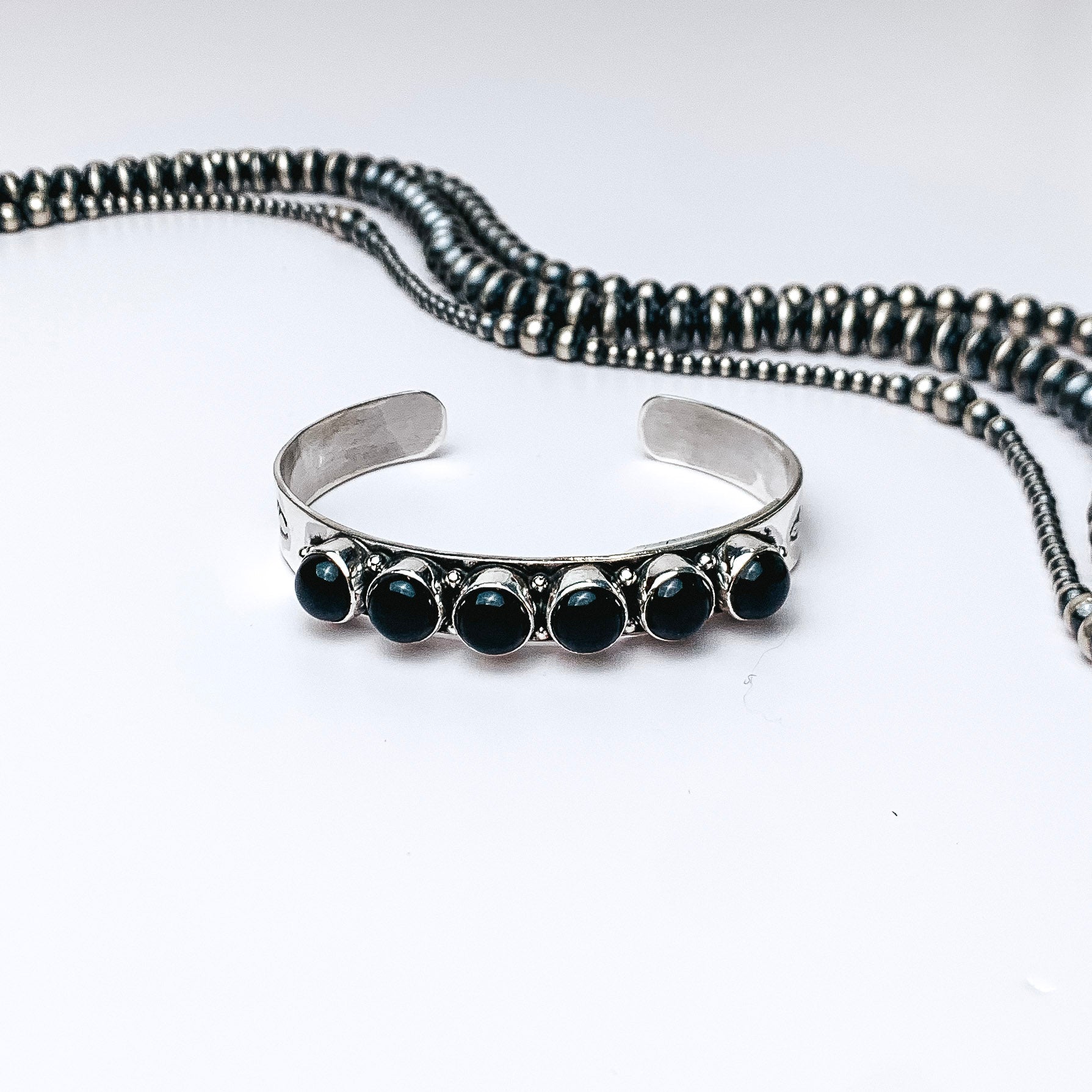 Centered in the picture is a cuff with six black onyx stones. Navajo pearls are laid above the cuff, all on a white background.