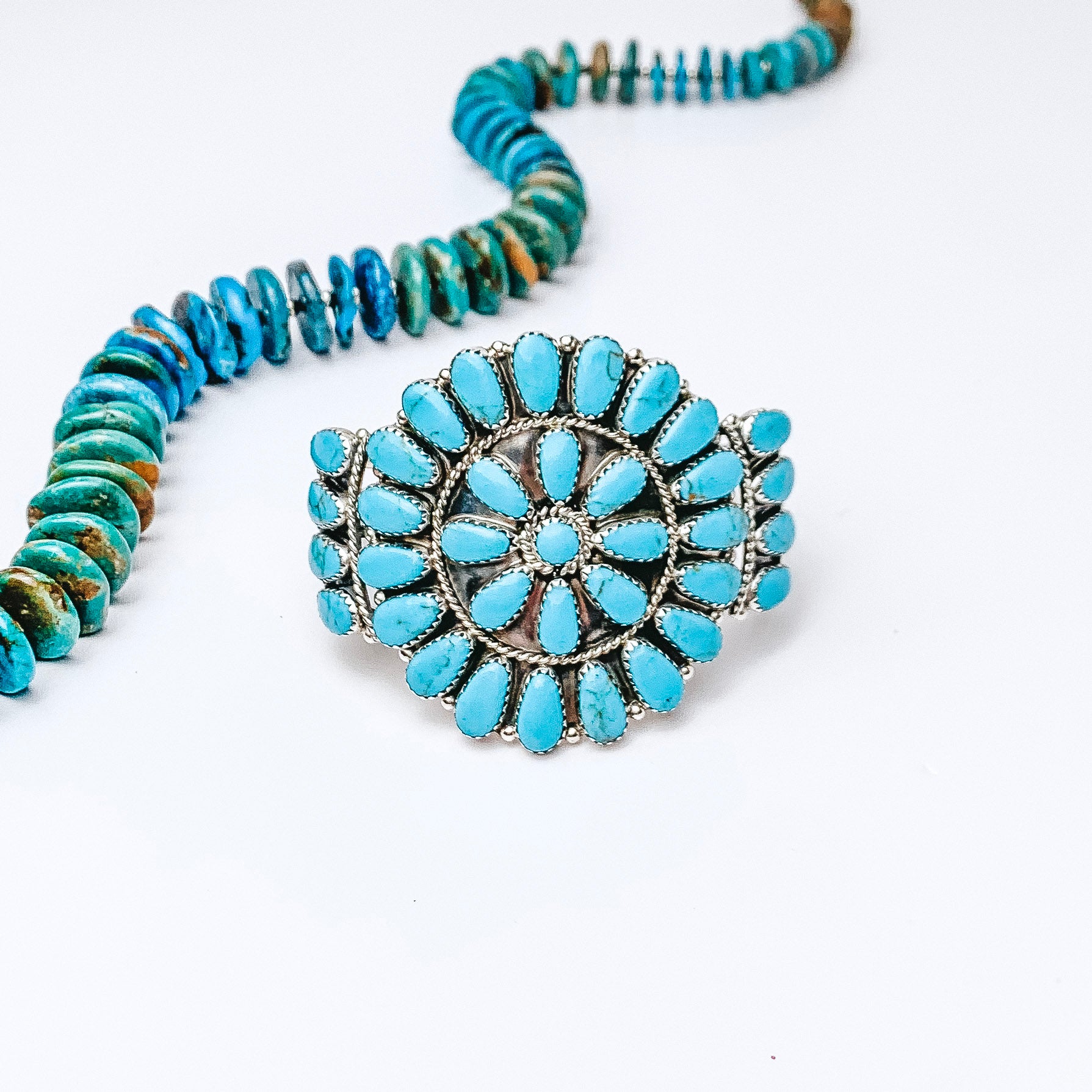 Centered is a turquoise cluster cuff on a white background. A turquoise necklace is laid above the cuff. 