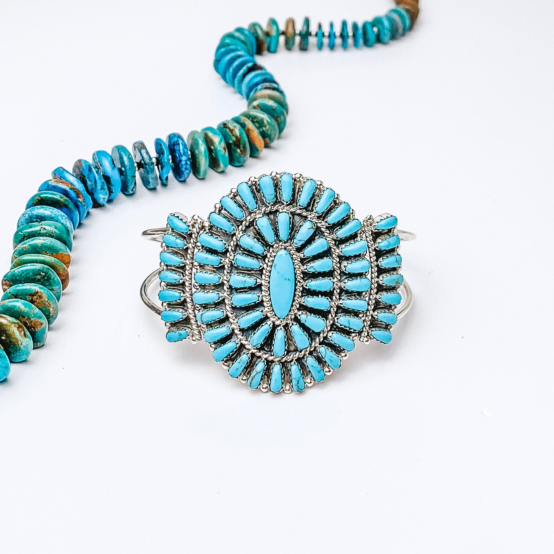 Centered in the picture is a turquoise cluster cuff with a turquoise necklace above the cuff. Background is all white.  