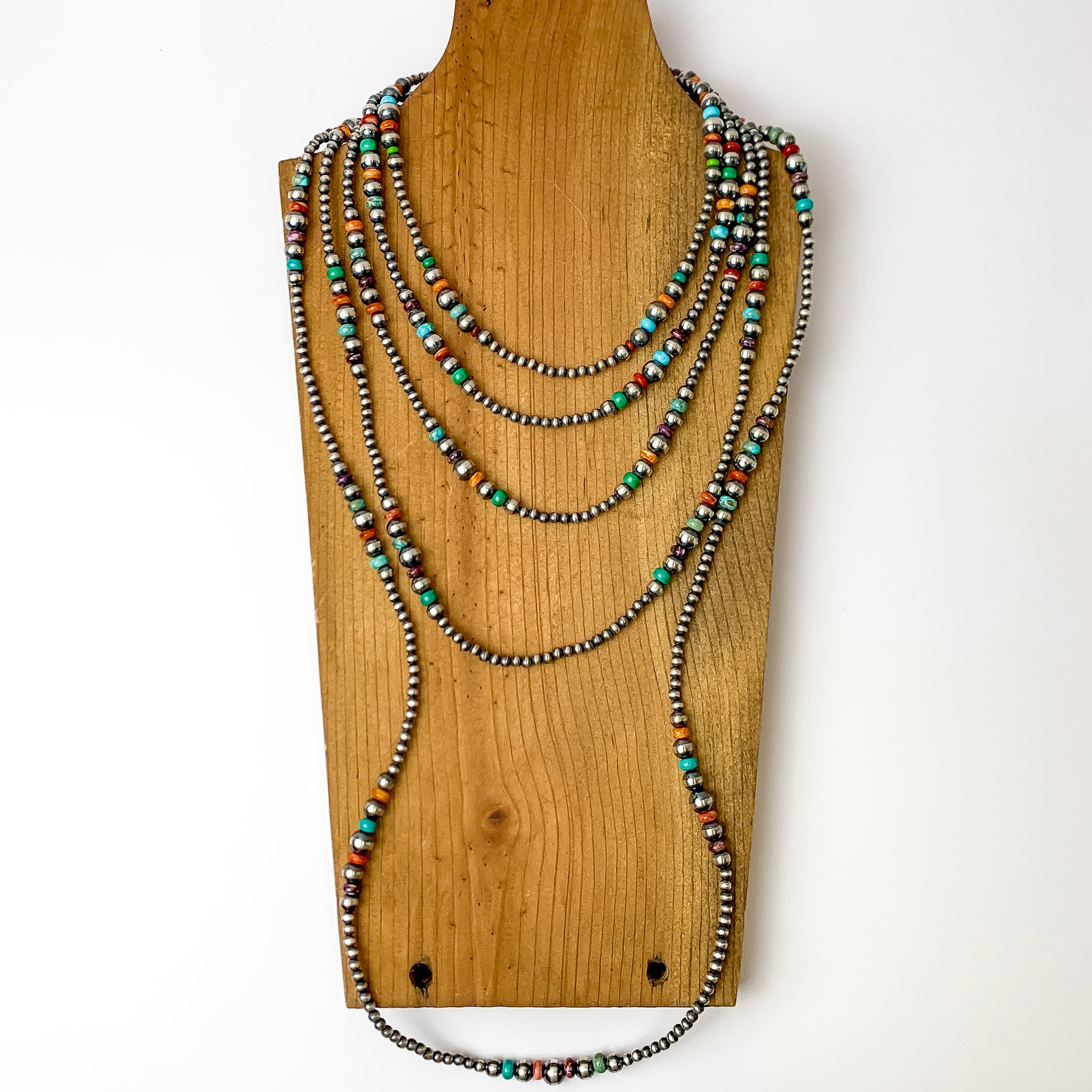 Navajo pearls are laid on a wooden necklace stand. Background is solid white. 