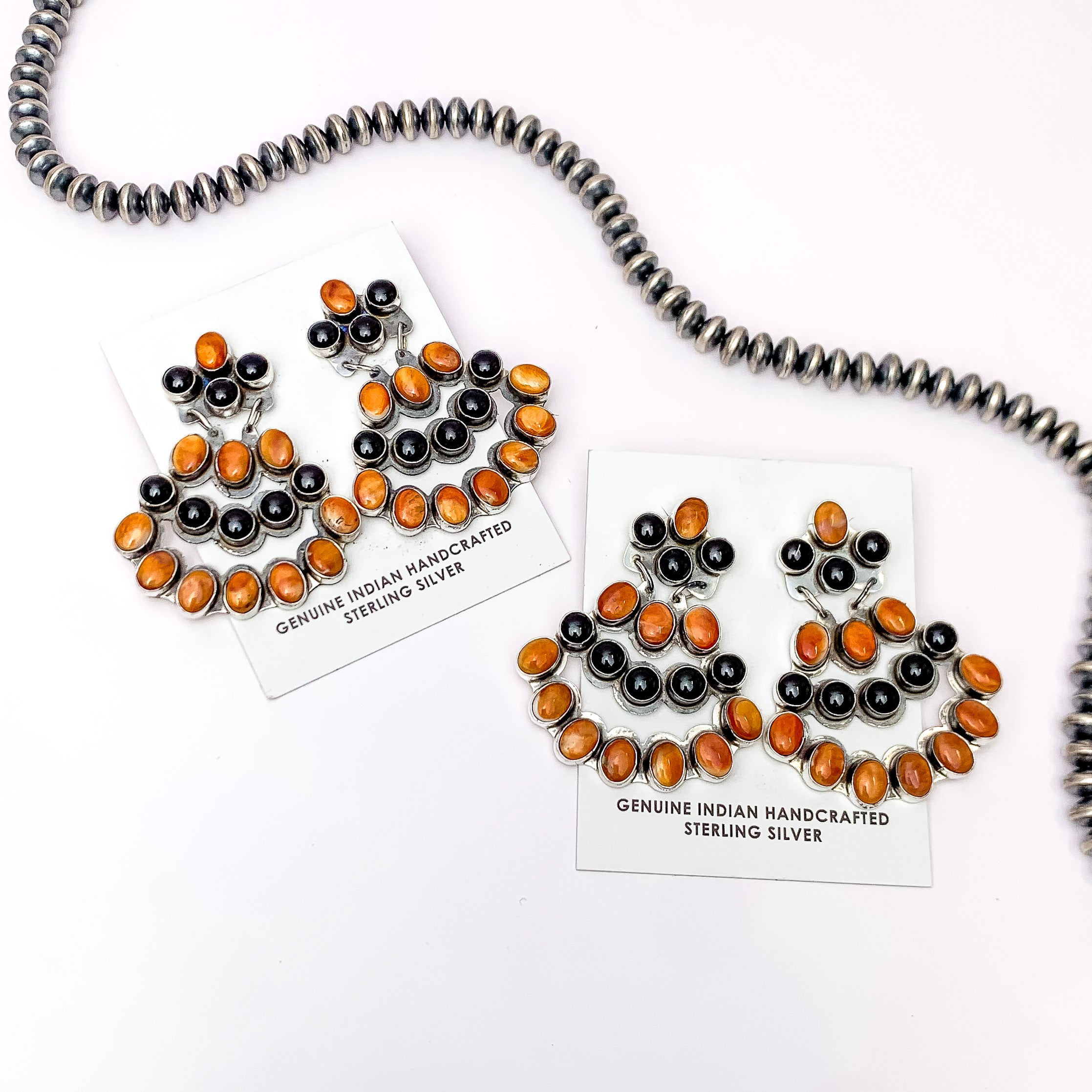 Centered in the picture is two pair of orange and black drop earrings on a white. 