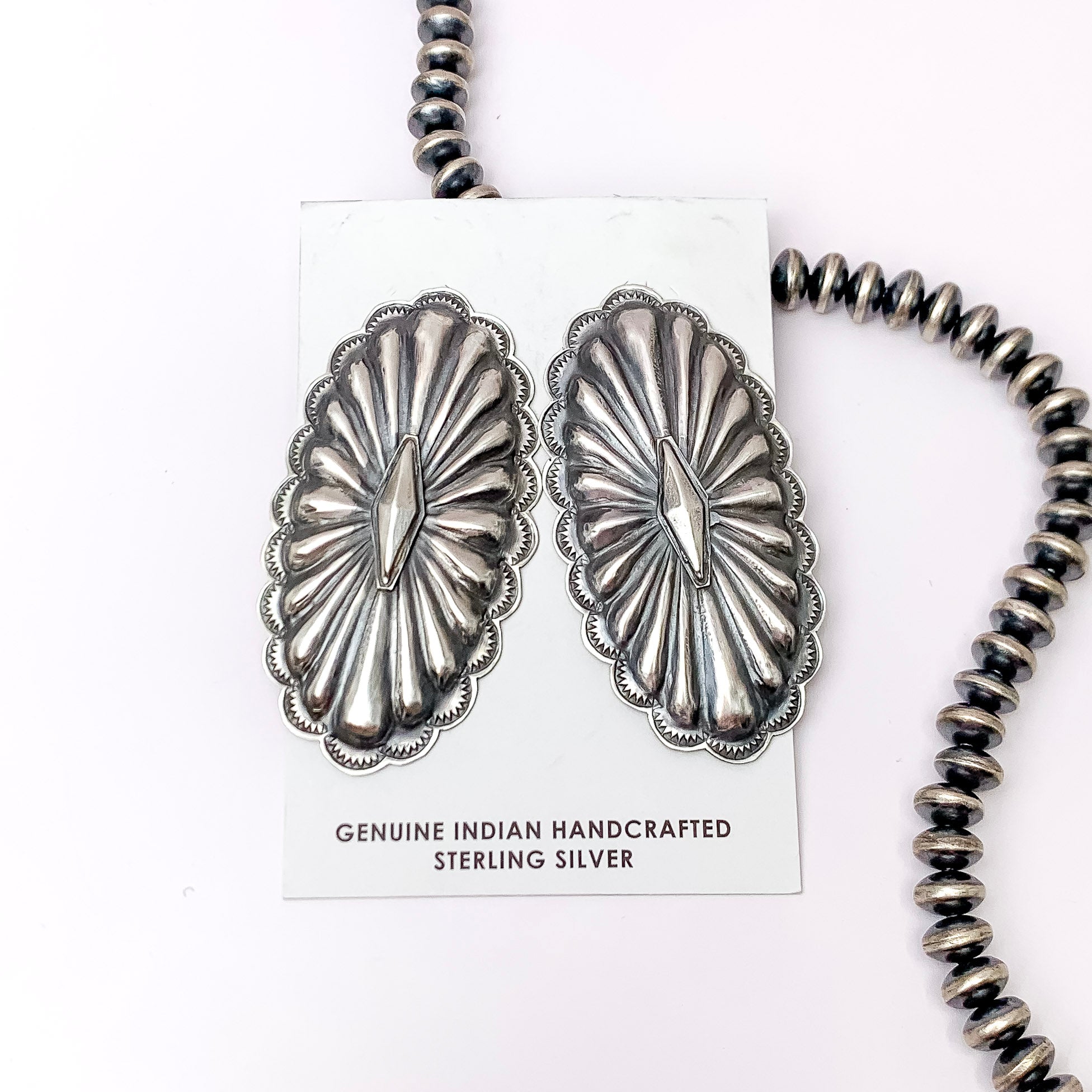Centered in the picture is a pair of oval concho earrings on a white background. 
