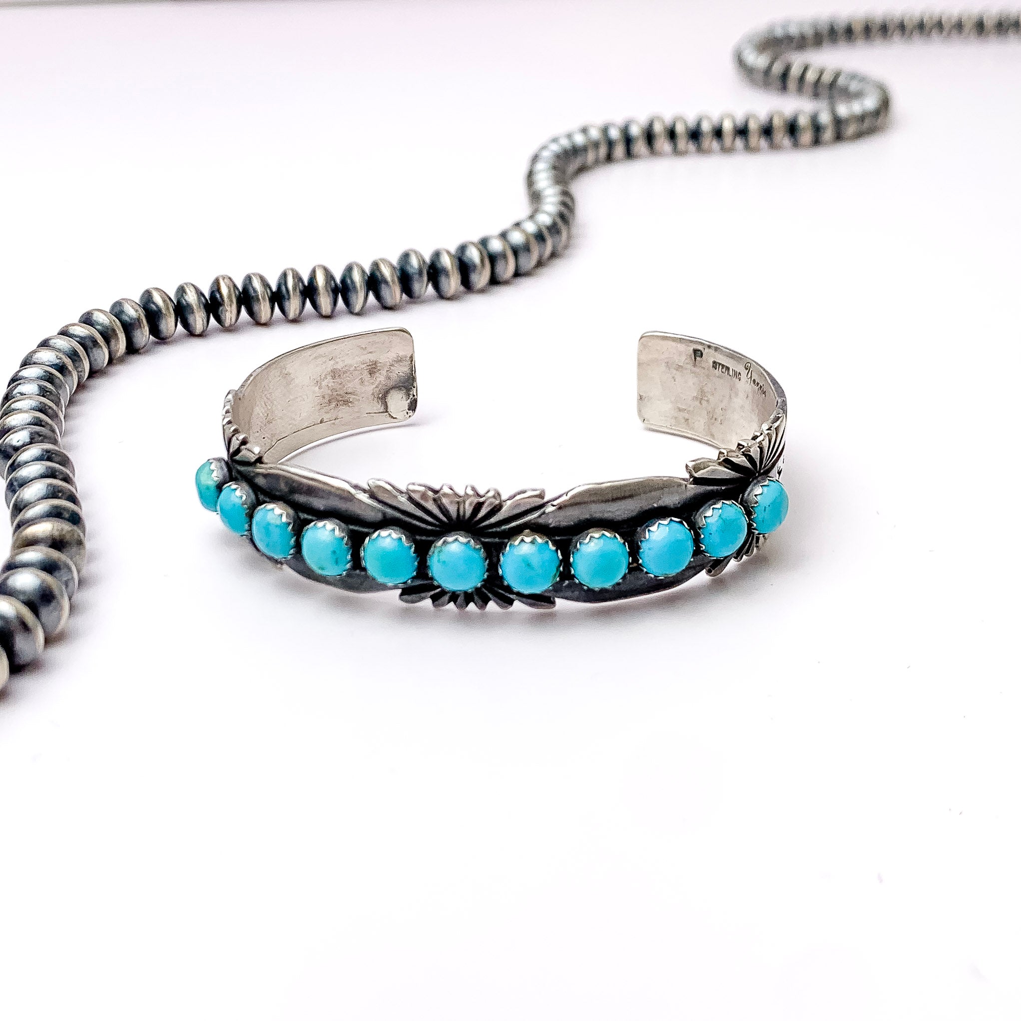 Centered in the picture is  a cuff bracelet with 11 turquoise stones on top of a tribal design. ALl on a white background. 