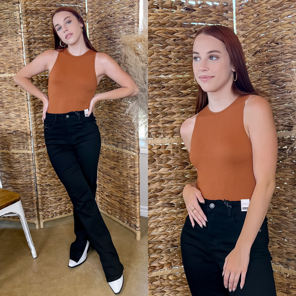 Model is wearing a ribbed, clay orange muscle tank body suit. Model is also wearing black jeans, white shoes, and gold hoops. 