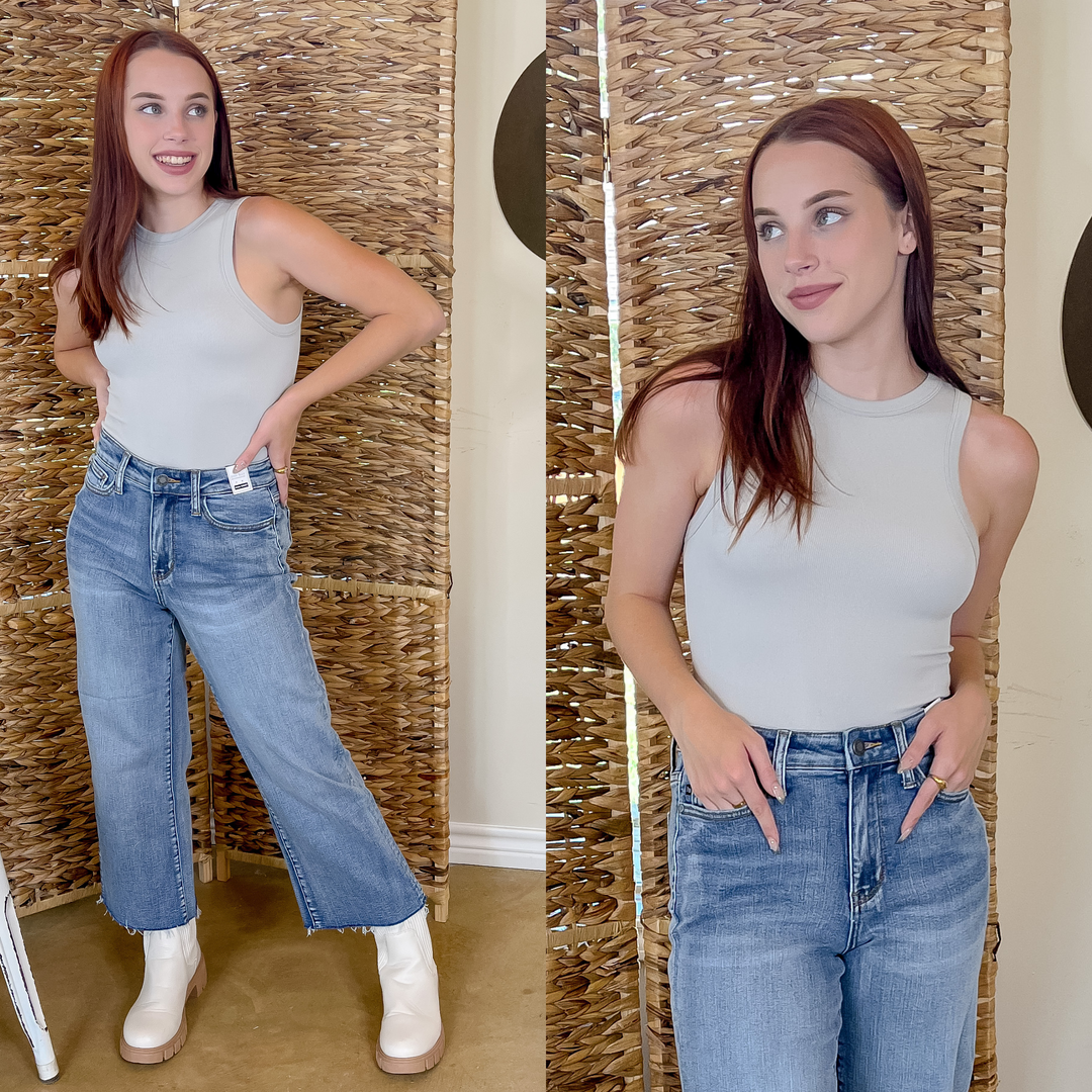 Model is wearing a grey, tank top body suit and flare denim jeans. Model is also wearing white boots with rubber soles.