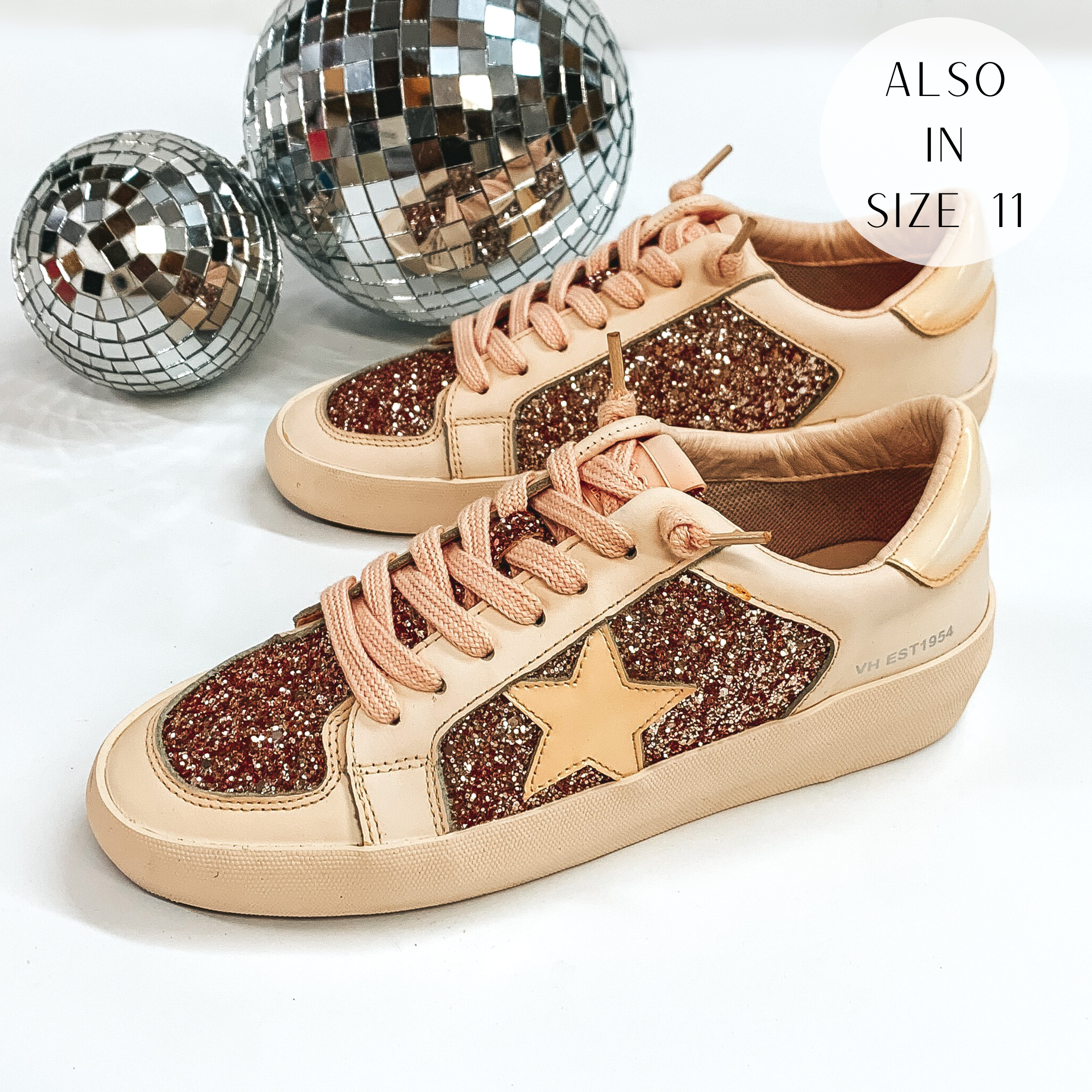Pictured are a beige colored pair of sneakers with rose gold glitter throughout. These shoes are pictured on a white background with disco balls in the background.