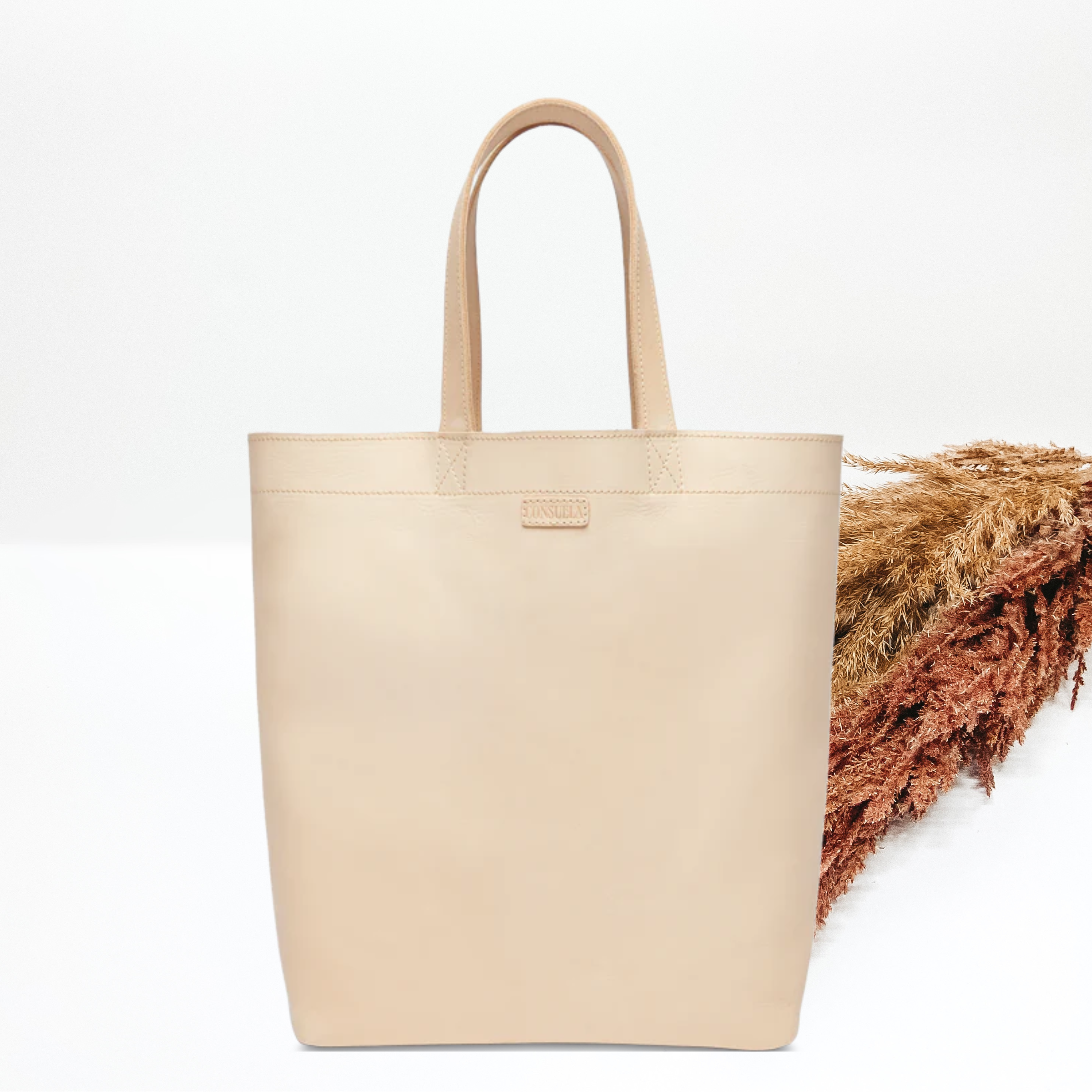 Light tan bag with the same colored handles. This bag is pictured in front of tan and brown pompous grass on a white background. 