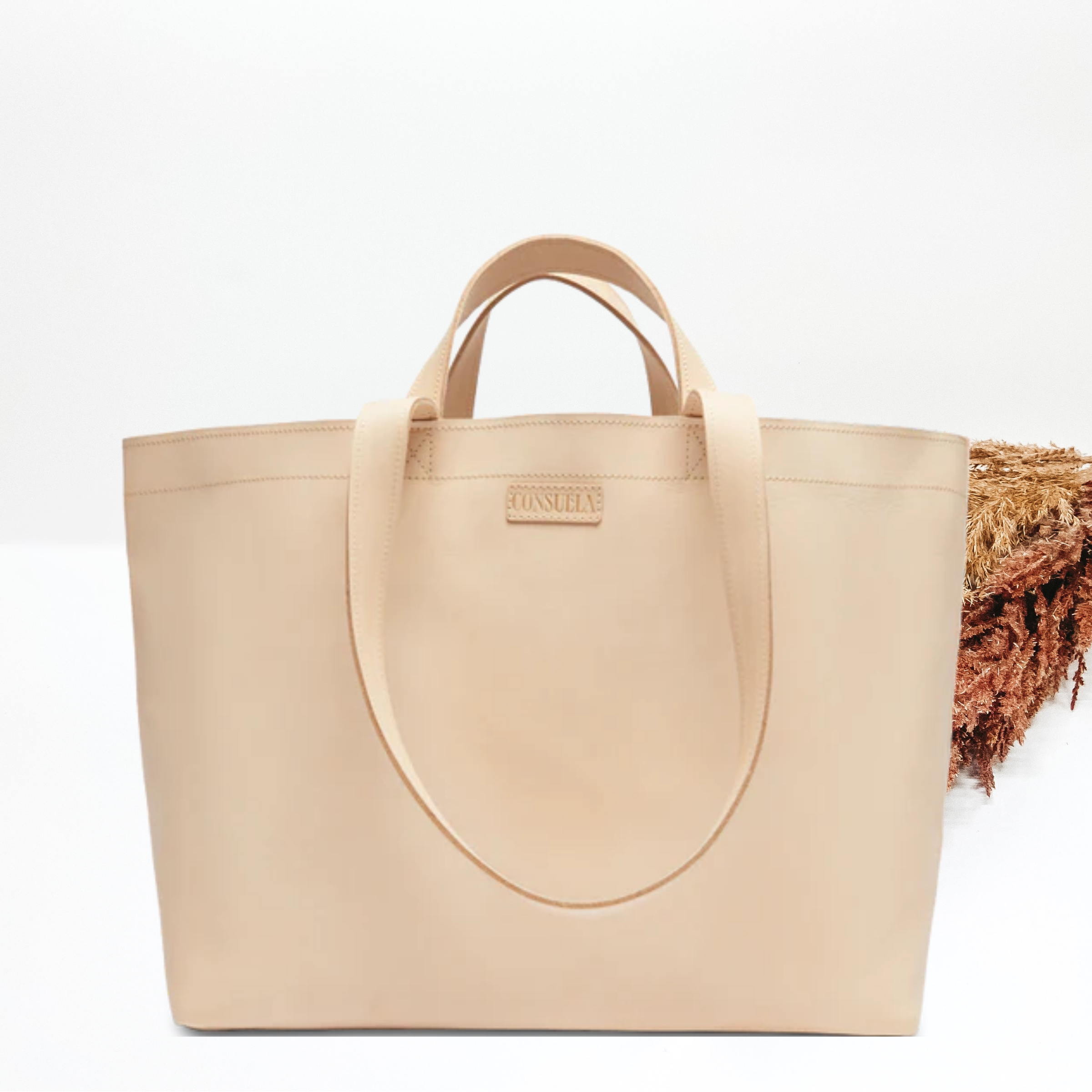 Light tan bag with the same colored handles. This bag includes a set of small handles an a set of longer handles. This bag is pictured in front of tan and brown pompous grass on a white background. 