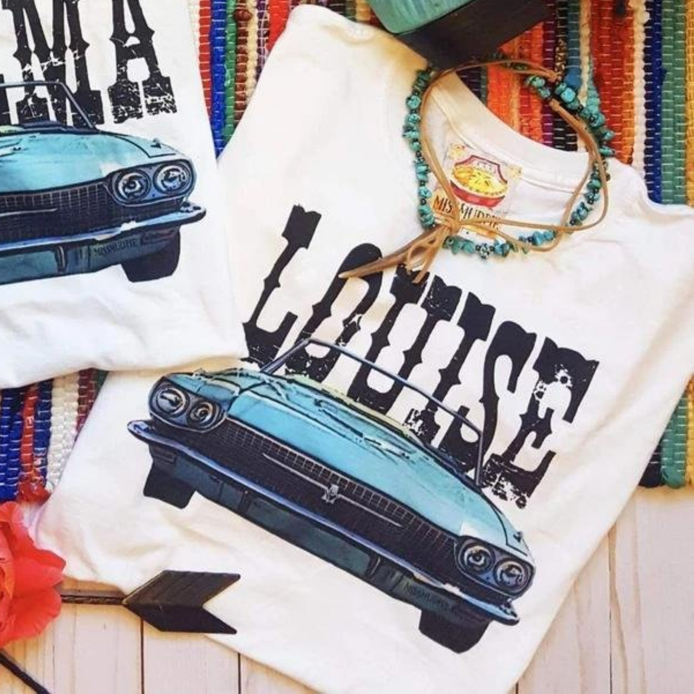 A white tee shirt folded into a rectangle exposing the vintage car graphic that says "Louise" above. Pictured with a turquoise necklace on a serape rug.