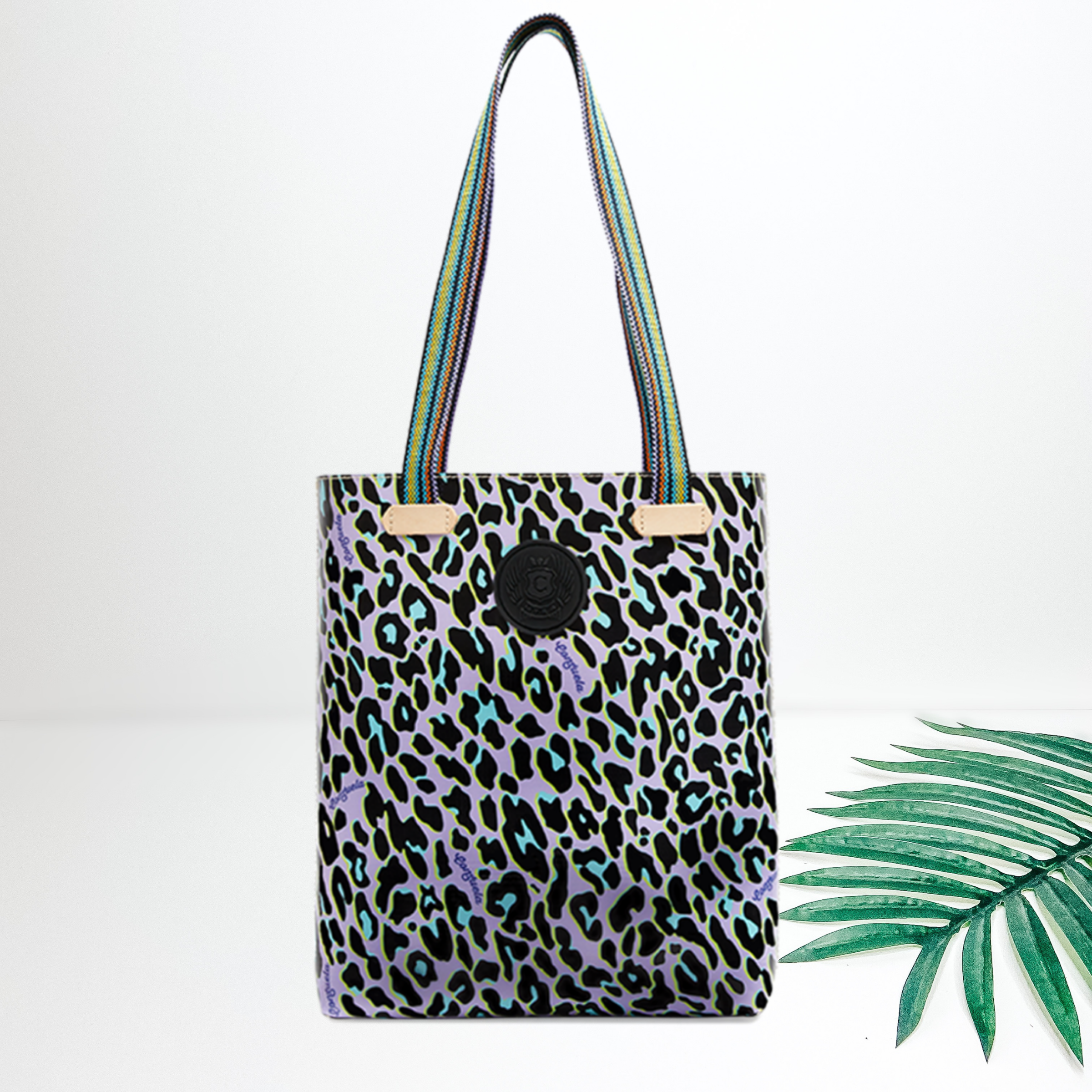 A large purple leopard print tote with long straps. Pictured on white background with a  palm leaf.