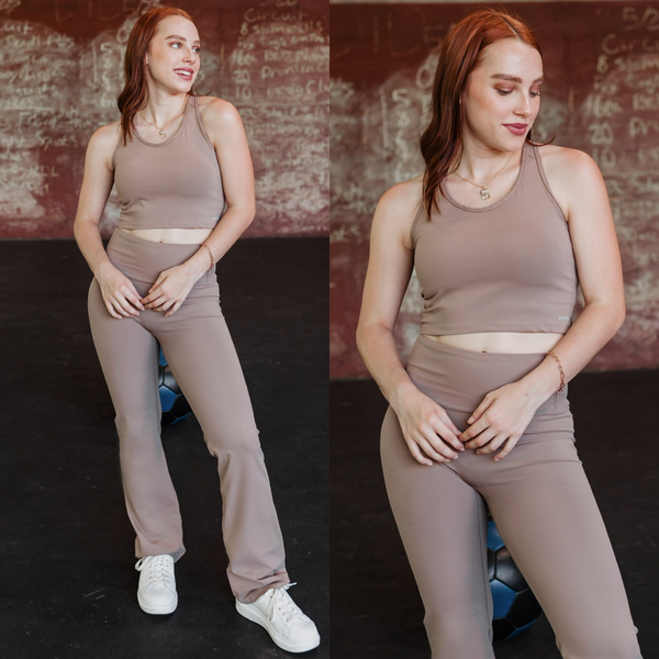 Model is wearing a taupe racer back sports bra. Model has it paired with matching taupe pants and white sneakers.