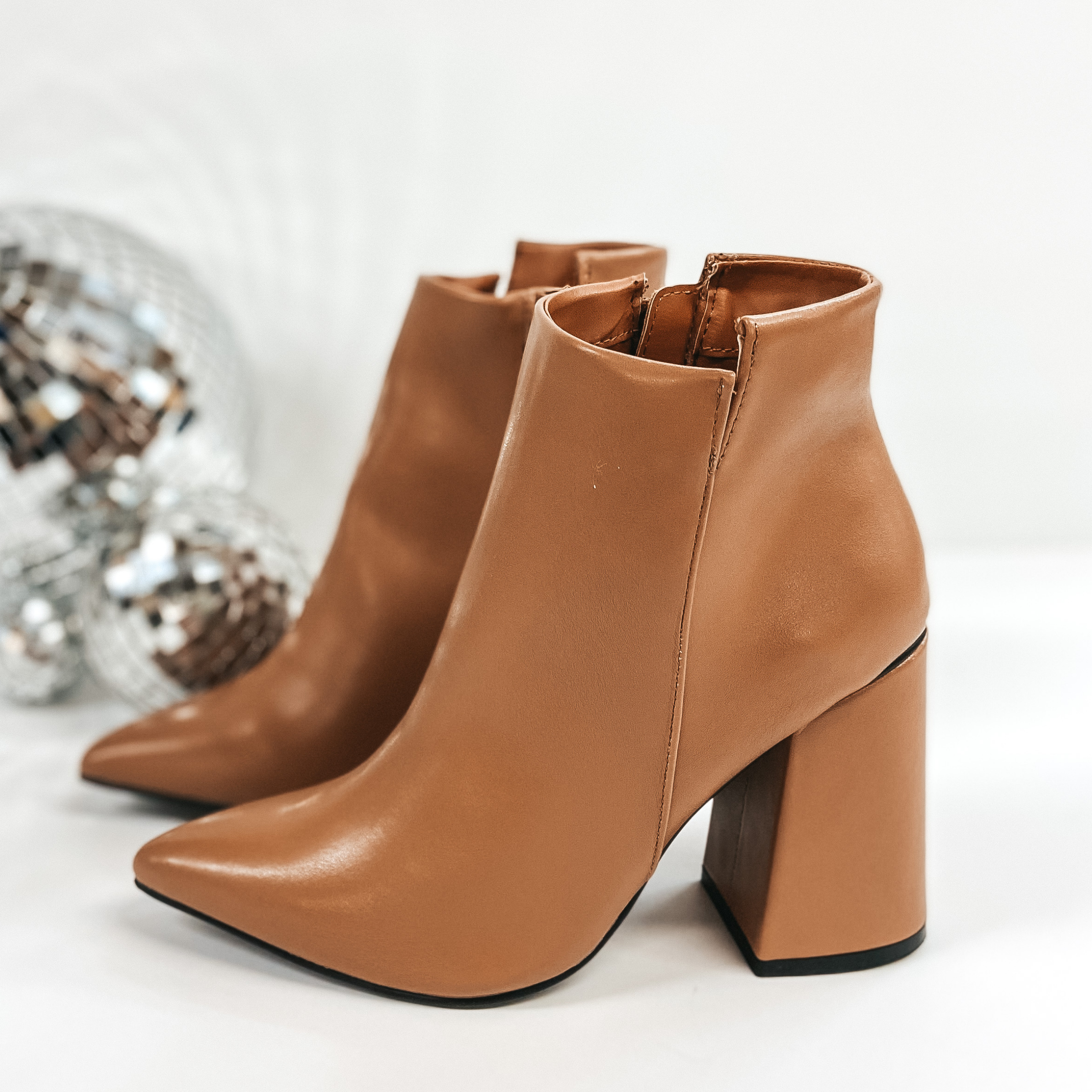 These booties have a high block heel with an asymmetrical ankle. The zip up booties have a pointed toe and are pictured on a white background with disco balls.