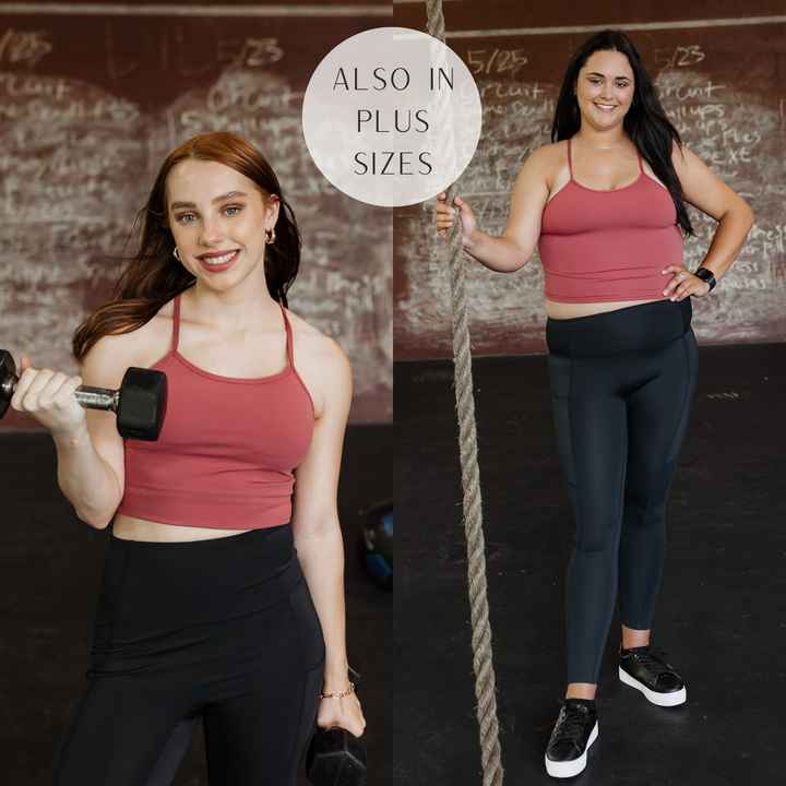 Models are wearing a rust red spaghetti strap sports bra. Both models have it paired with black leggings, black sneakers, and gold jewelry.