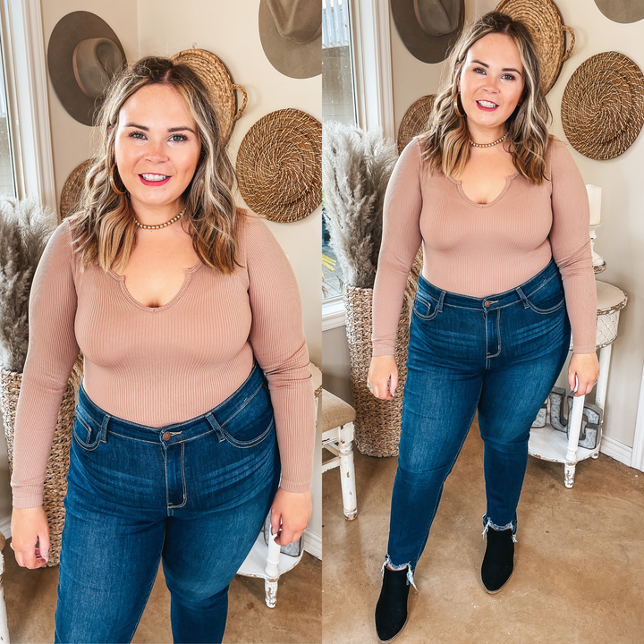 Model is wearing a notched neck tan top that is tucked into dark wash skinny jeans with black booties and gold jewelry.