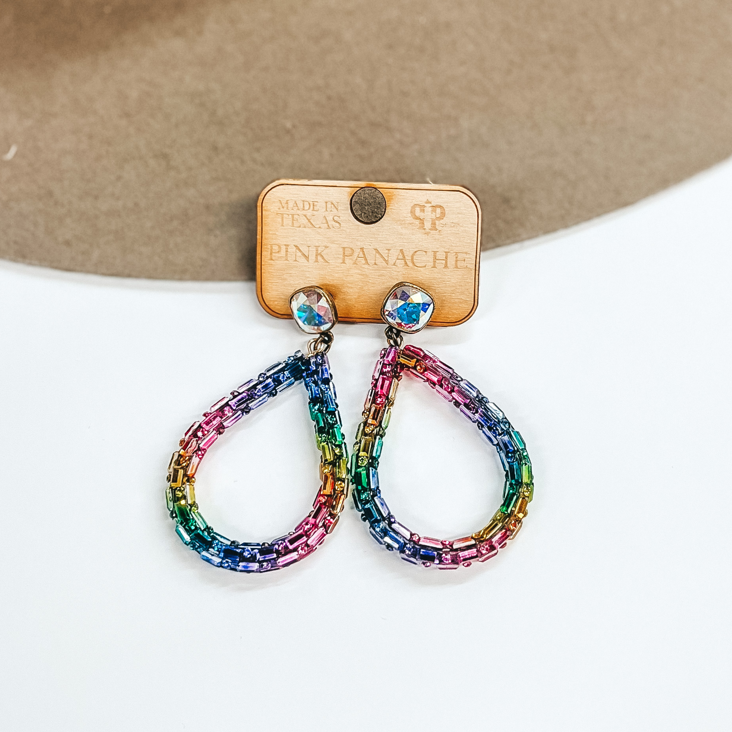 AB cushion cut crystal studs with hanging teardrop dangle. The teardrop dangle has a rainbow of colors. These earrings are pictured on a brown and white background. 