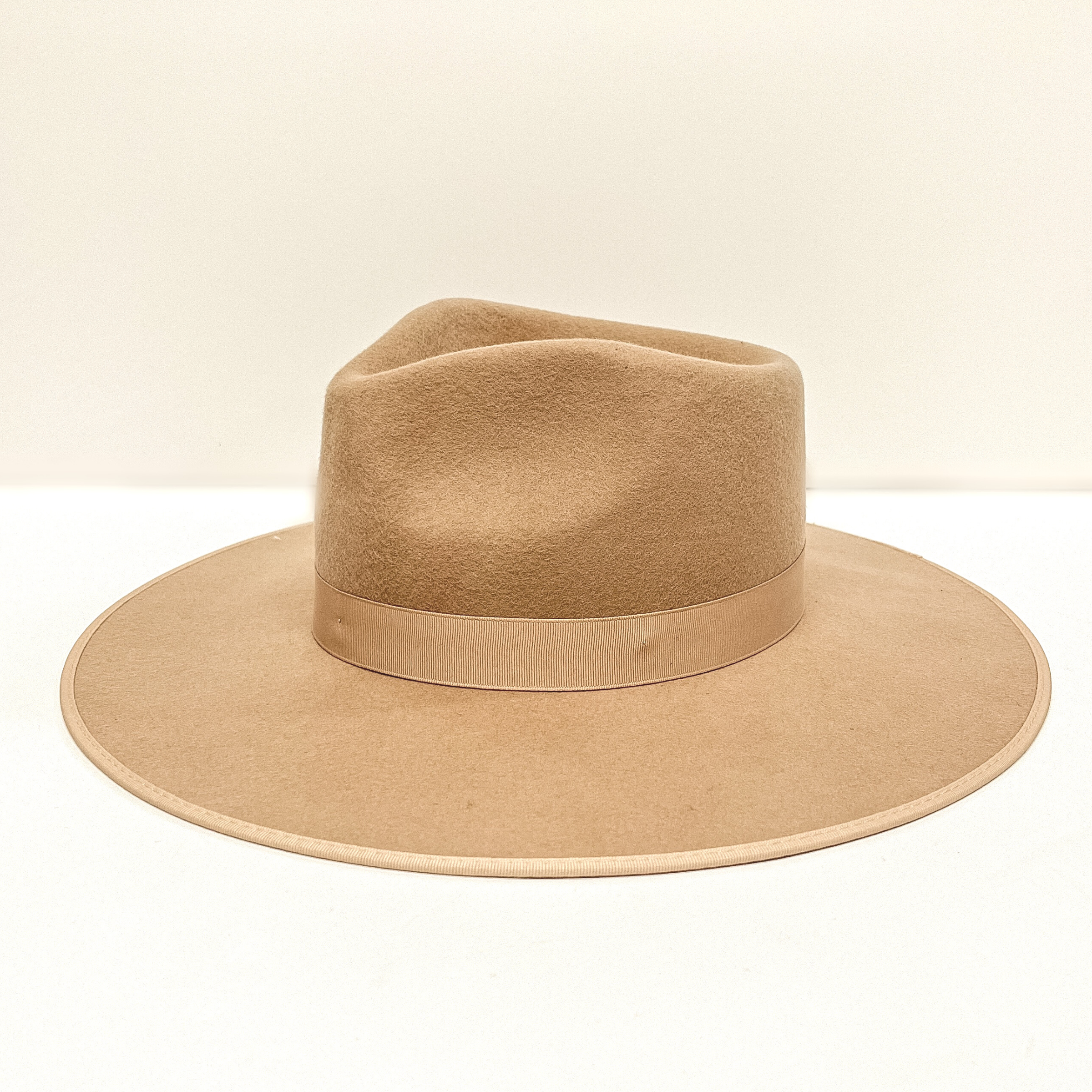 A light brown hat that has a ribbon band pictured on a white background.