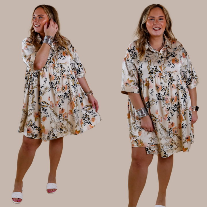 Model is wearing an ivory satin dress with a collared neckline, short sleeves, button up front, and floral and animal print pattern. Model has it paired with white heels and silver jewelry.