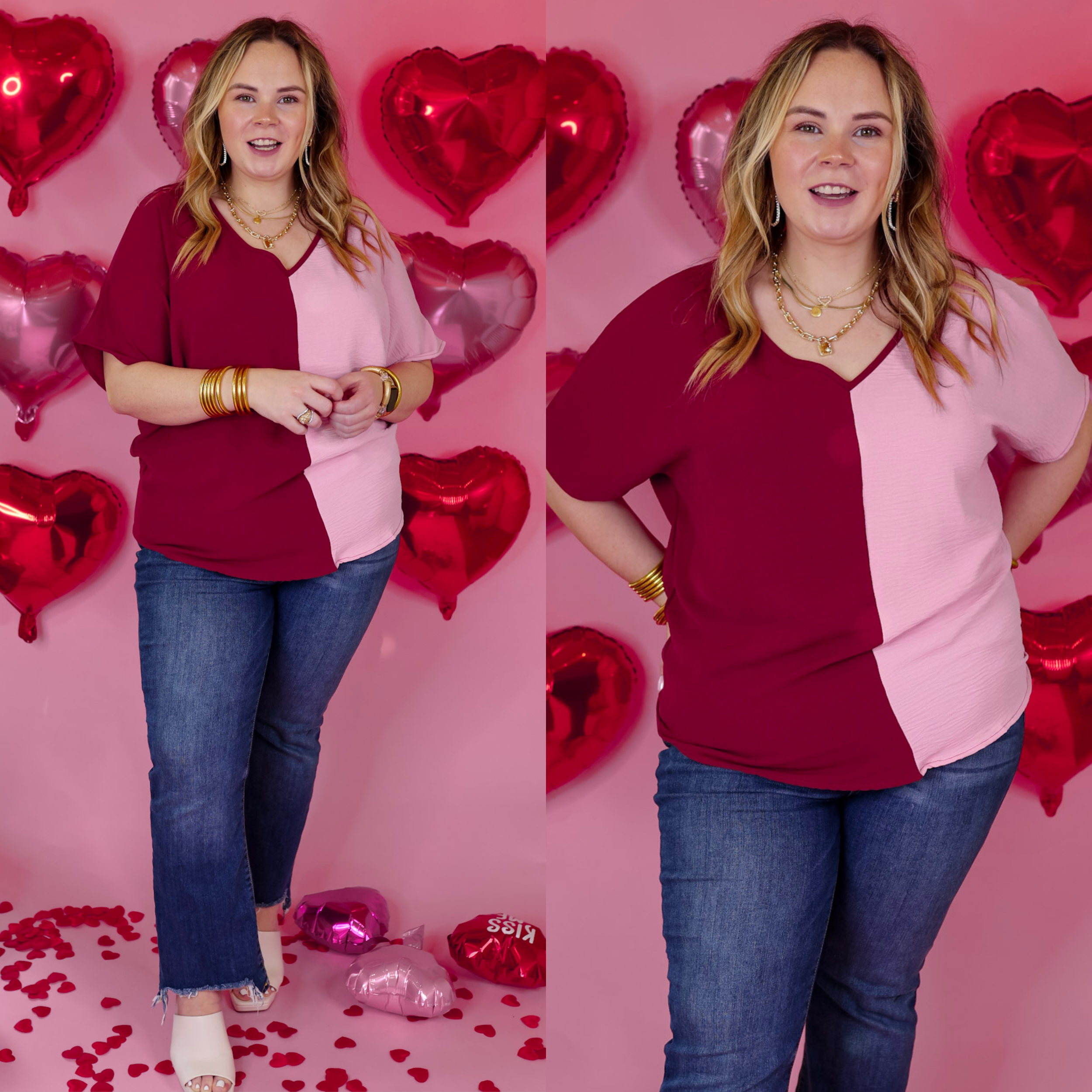 Model is wearing a short sleeve v neck top in maroon and light pink. Model has this top paired with straight leg jeans, white heels, and gold jewelry. Background is light pink with red heart balloons. 