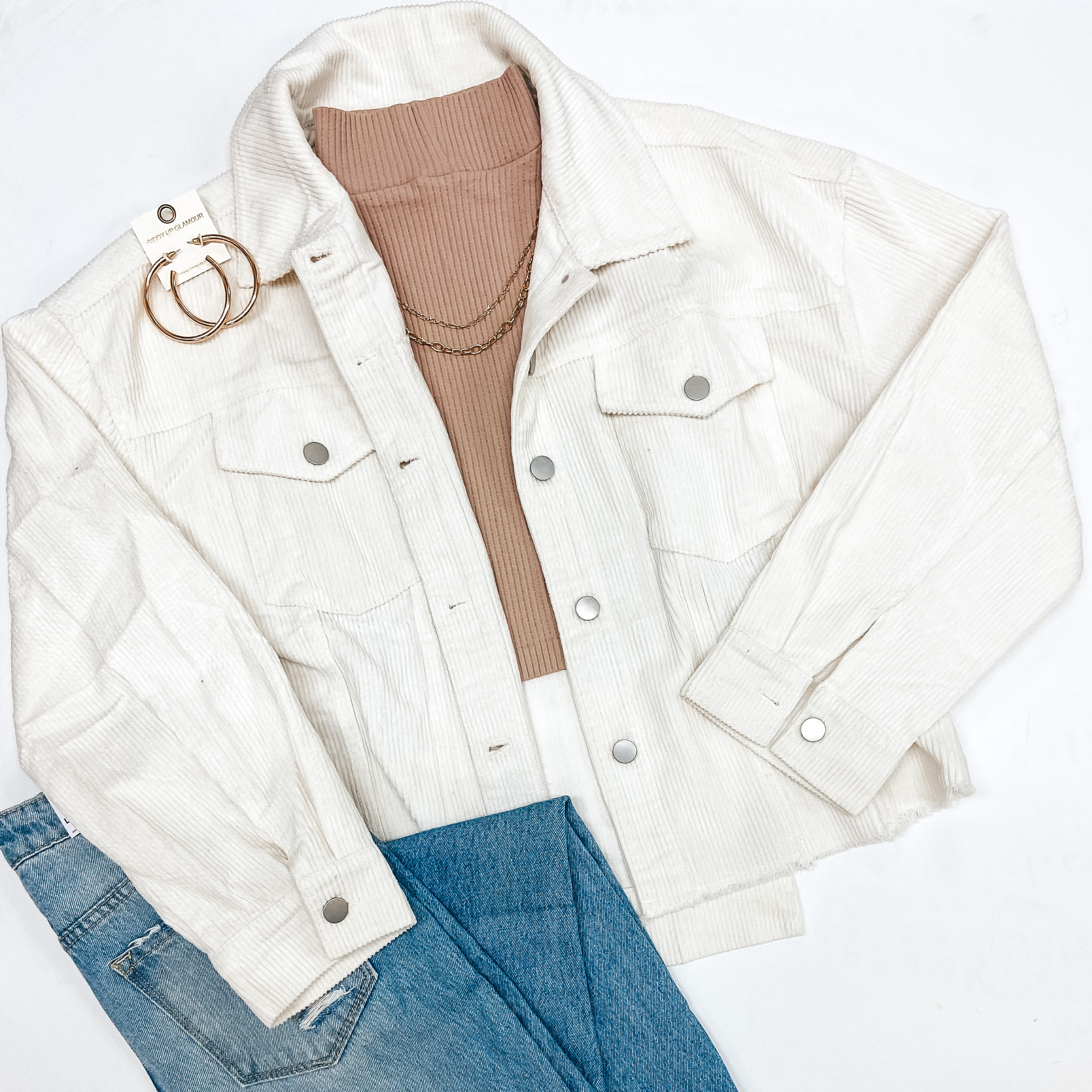 An ivory corduroy shacket pictured with a taupe turtle neck, blue jean, and gold jewelry.