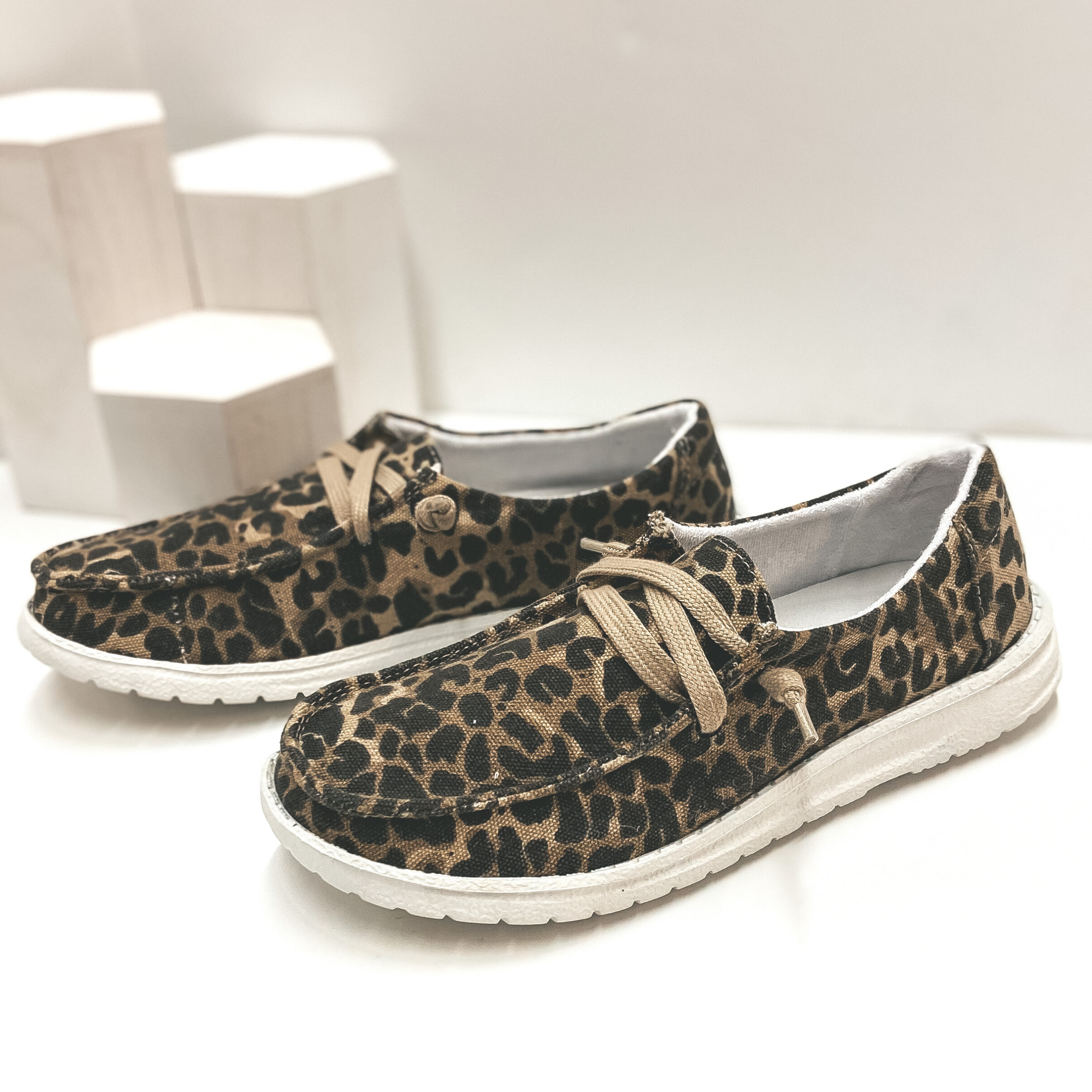 Leopard print slip on loafers with a taupe colored shoe lace and white sole. Pictured on white background.