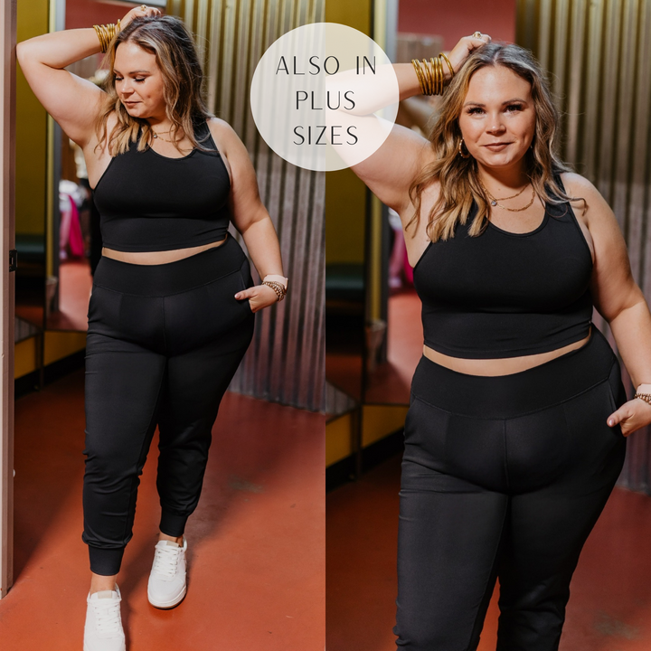 Model is wearing a black tank top sports bra that has an open back. Model has it  paired with black joggers, white sneakers, and gold jewelry.