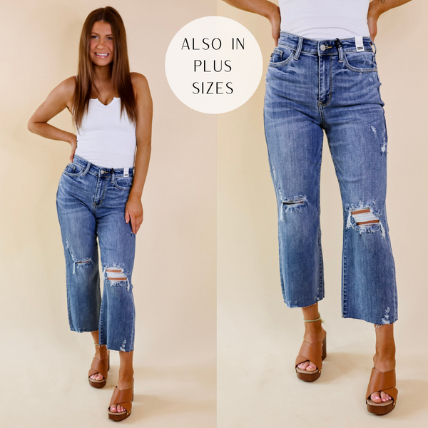 Model is wearing a pair of distressed wide leg jeans that have a cropped hem. Model has these jeans paired with tan wedges and a white tank top.