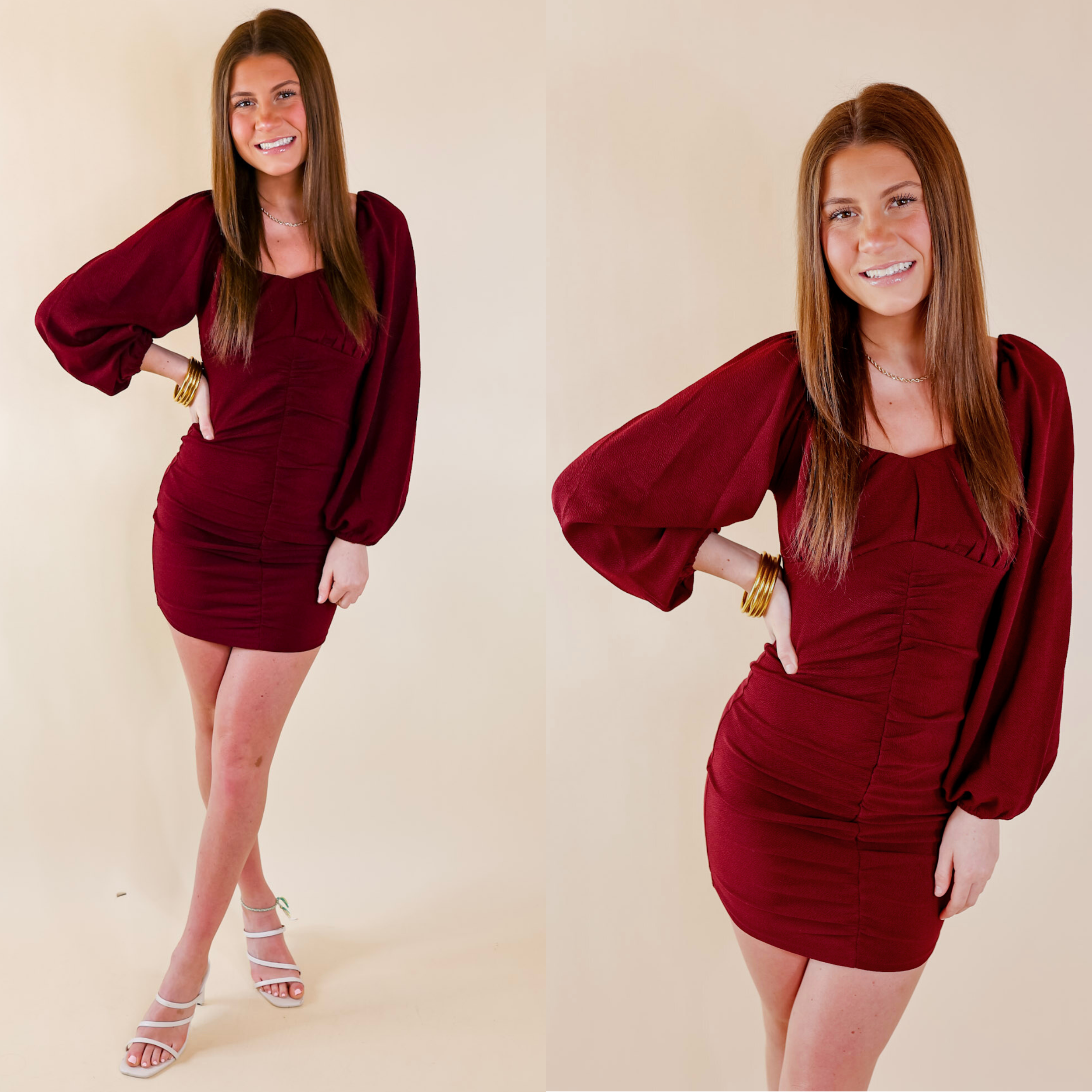 Model is wearing a maroon dress with ruching up the front,  and long balloon sleeves. Model has it paired with white heels and gold jewelry.