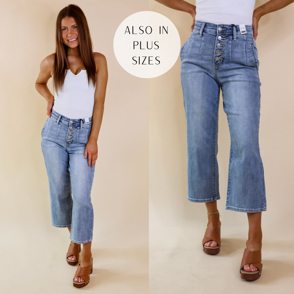 Model is wearing a pair of wide leg jeans that are cropped with a button fly. Model has these jeans paired with tan wedges and a white tank top.