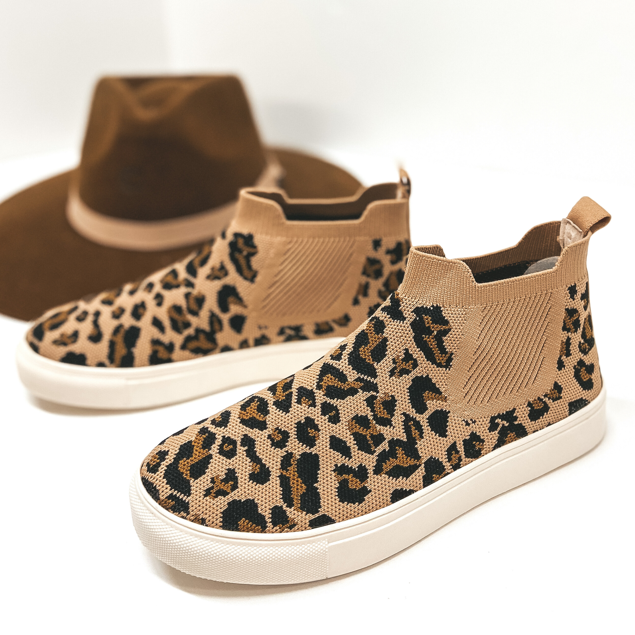 High top knit leopard sneakers in a leopard print. Shoes are pictured on white background with a brown rancher hat.
