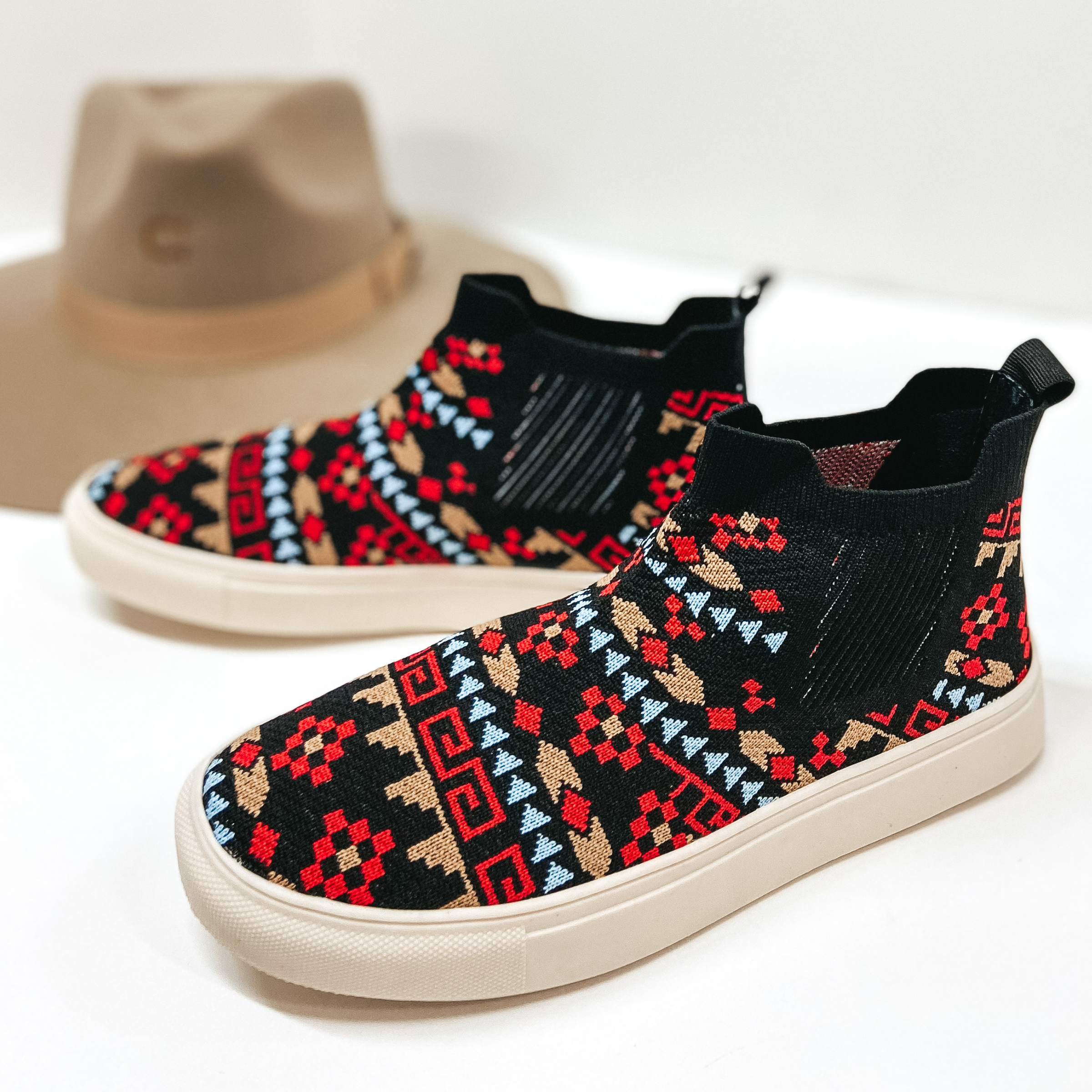 Black knit high top sneakers with red, blue, and taupe tribal designs. Pictured on white background with tan hat.