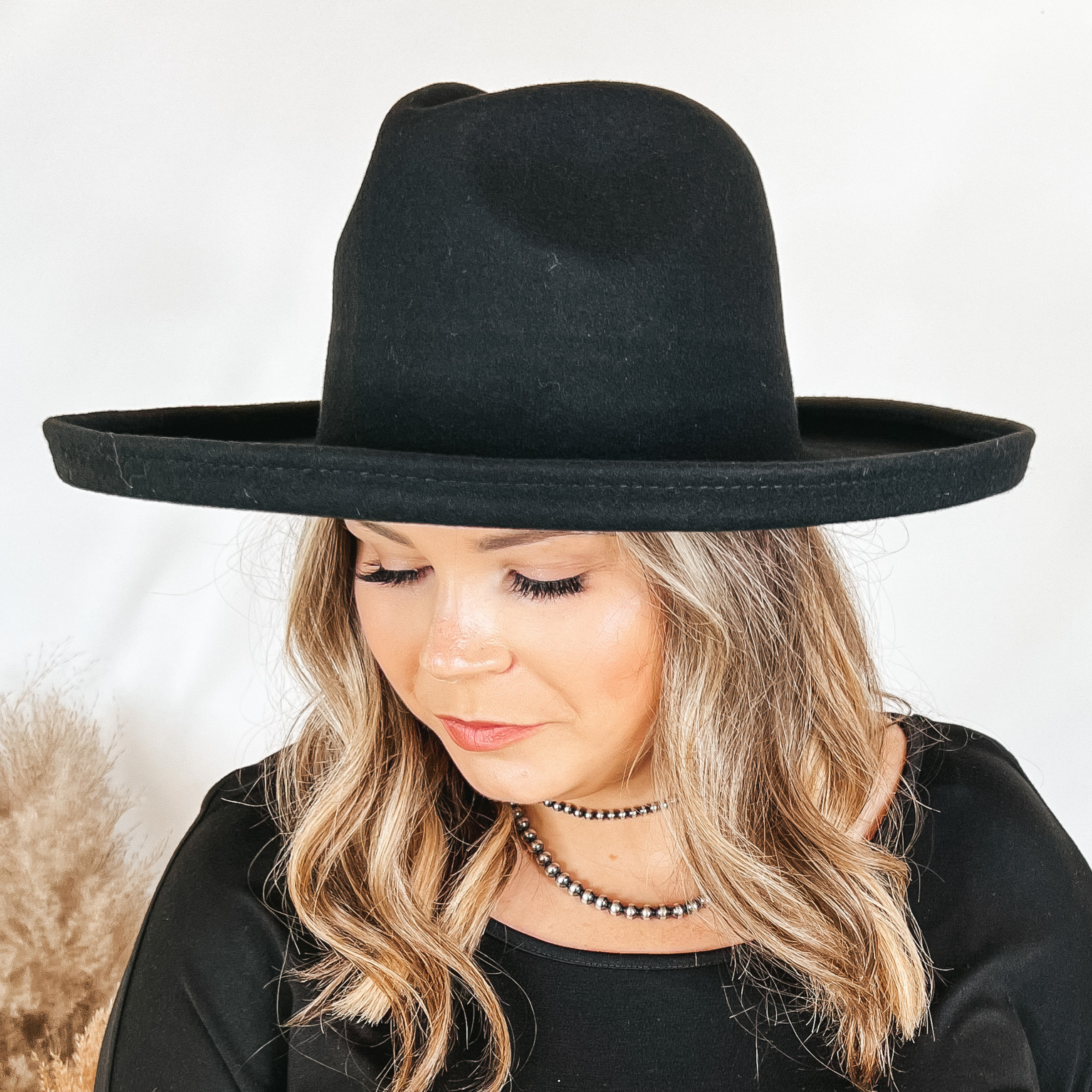 Model is wearing a black felt hat with a flat brim and a pencil curve end. 