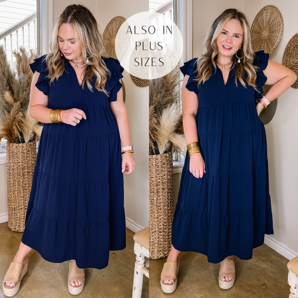 Model is wearing a navy midi dress with ruffle cap sleeves and a notched neckline. Model has it paired with tan wedges and gold jewelry.