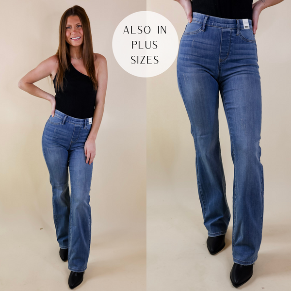 Model is wearing a pair of jeans with an elastic waistband, faux front pockets, and a slim boot leg. Model has these medium-wash jeans paired with black booties and a one shoulder top.