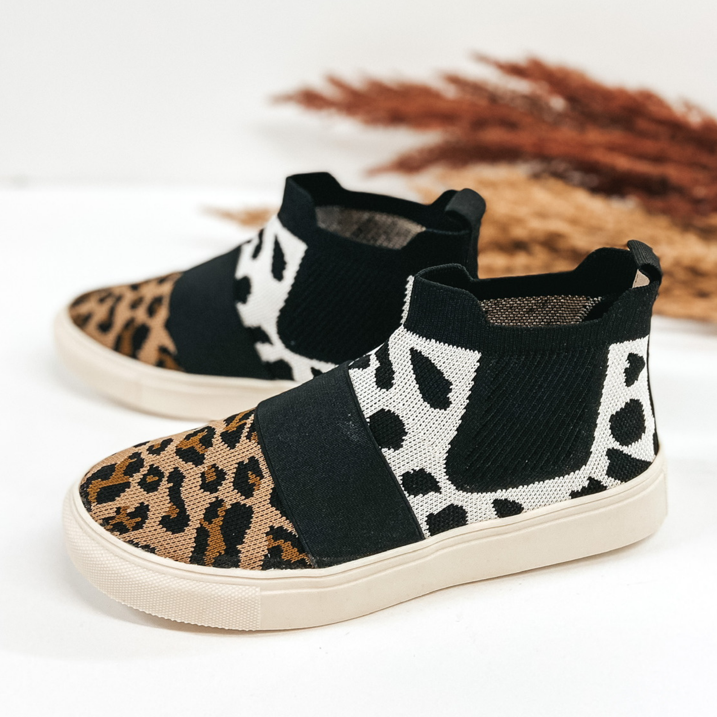 High top knit sneakers that are a white dotted print on the upper and a leopard print around the toe. Pictured on white background with pampus grass.