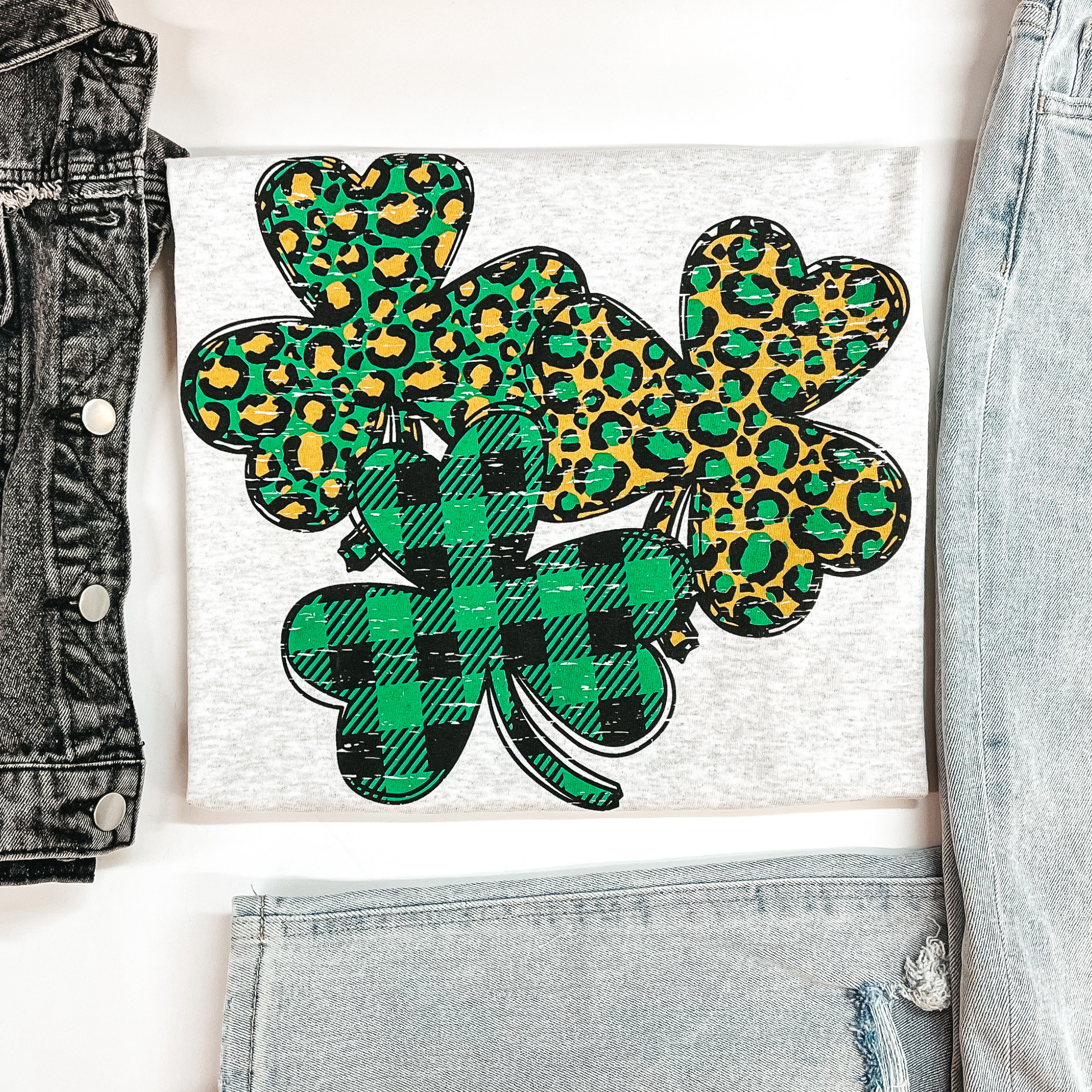A grey graphic tee folded to expose the graphic of leopard print and plaid clovers.