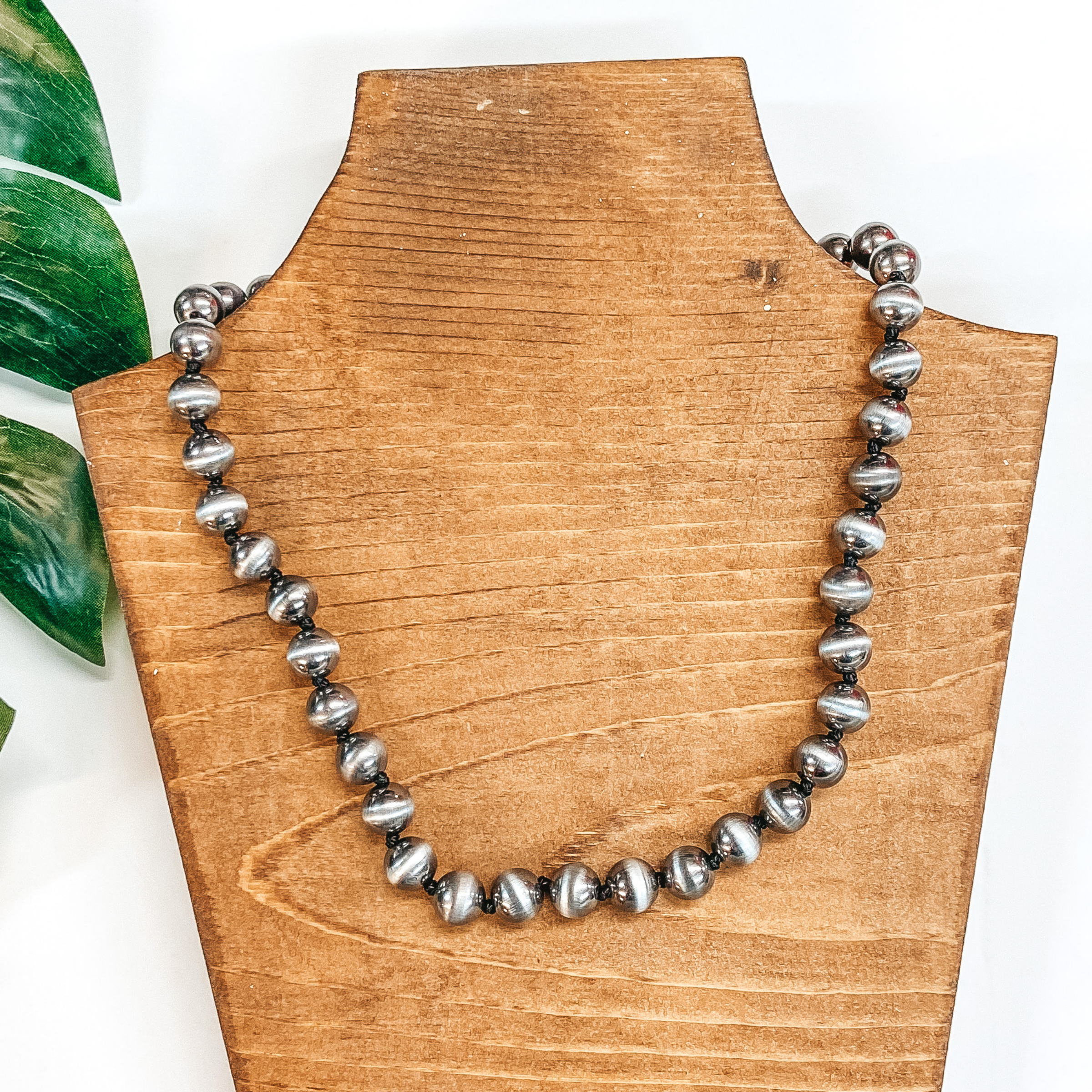 A silver faux Navajo Pearl necklace pictured on a white background with a palm leaf.