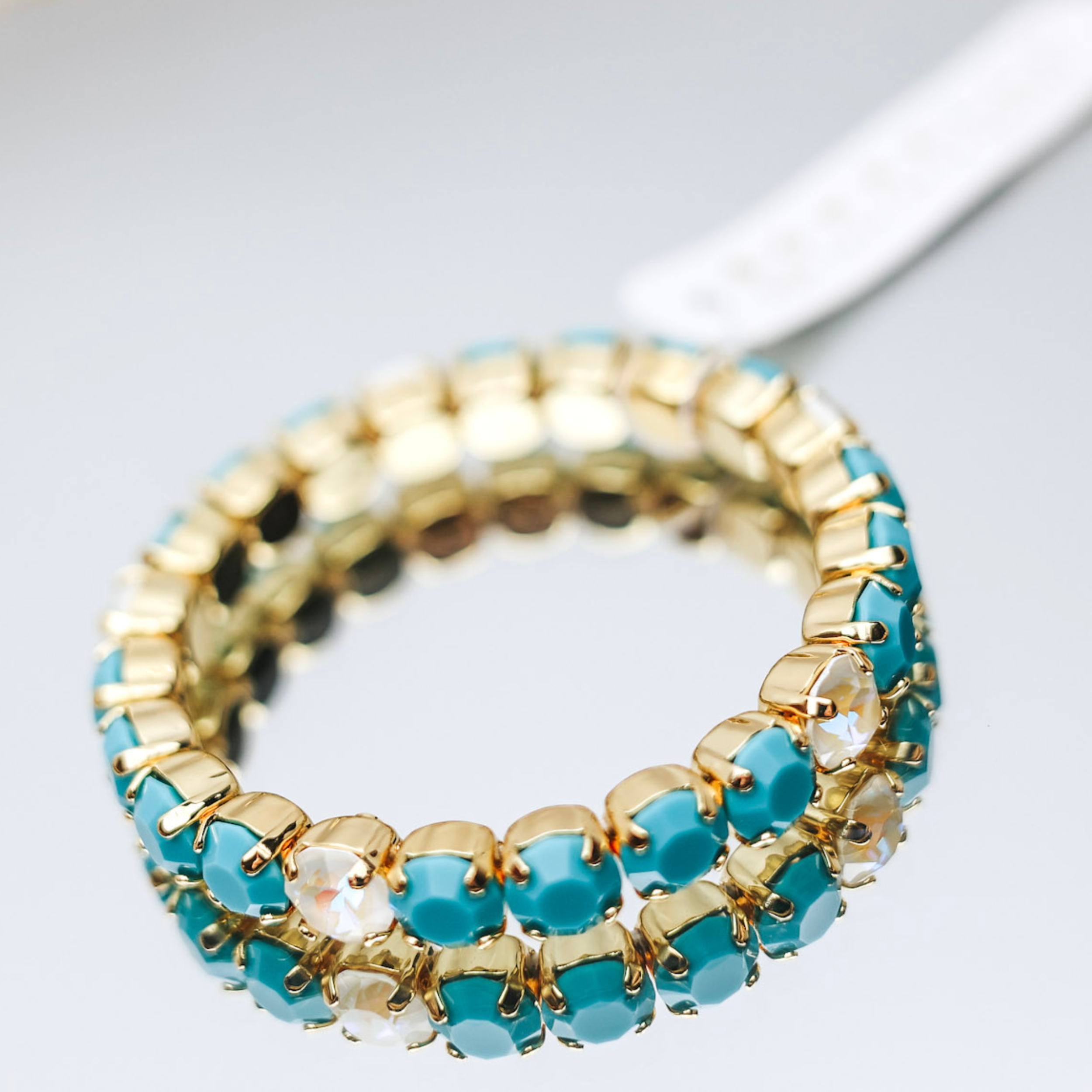 A gold-tone bracelet with crystals in turquoise blue and ivory, pictured on a mirror.