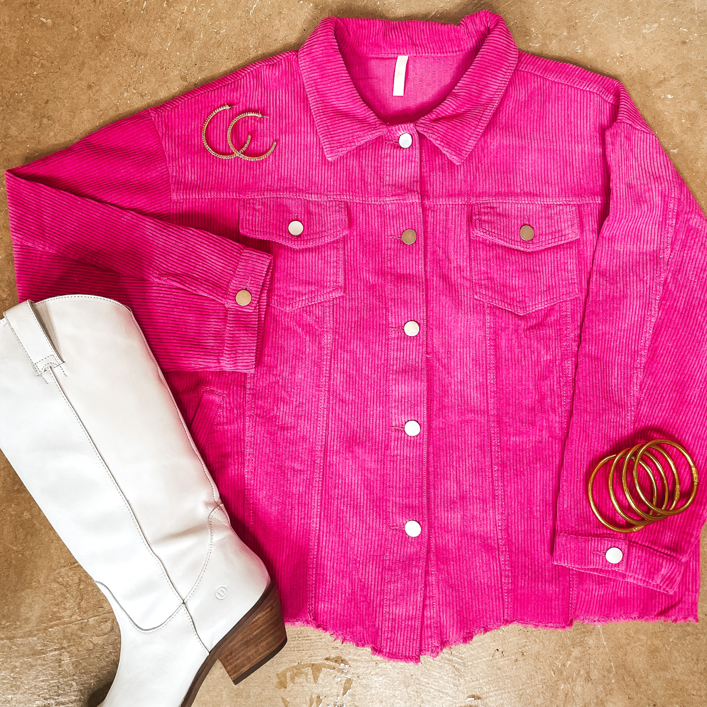 A hot pink corduroy shacket pictured on a concrete background with white boots and gold jewelry.