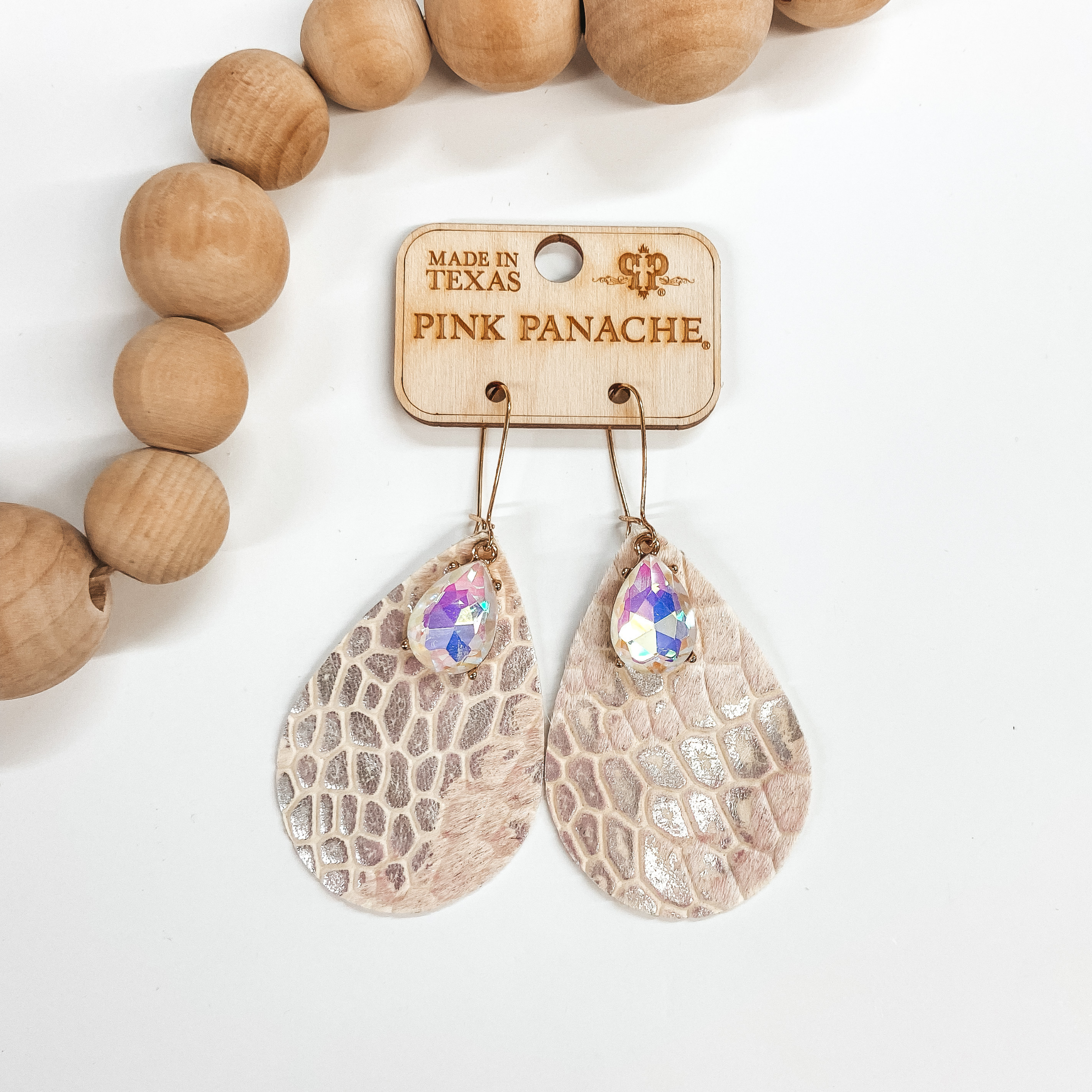 A pair of teardrop shaped earrings that are a white metallic crocodile print. These earrings have a teardrop shape crystal. Pictured on white background with wooden beads.