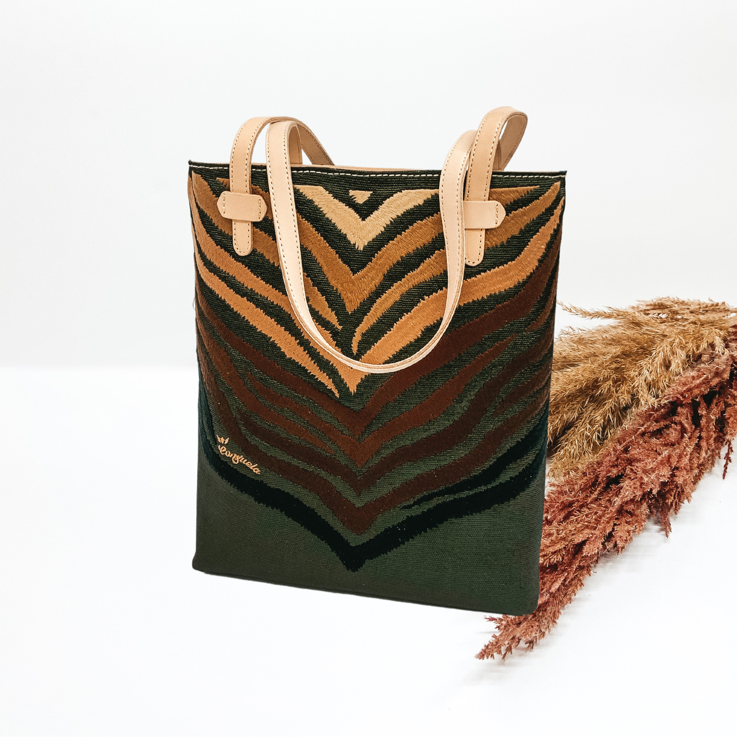 Tall, rectangle, green bag with a embroidered zebra print design. The zebra print goes from beige to black. This bag also has tan leather straps. This purse is pictured on a white background with tan and brown pompous grass in the background.