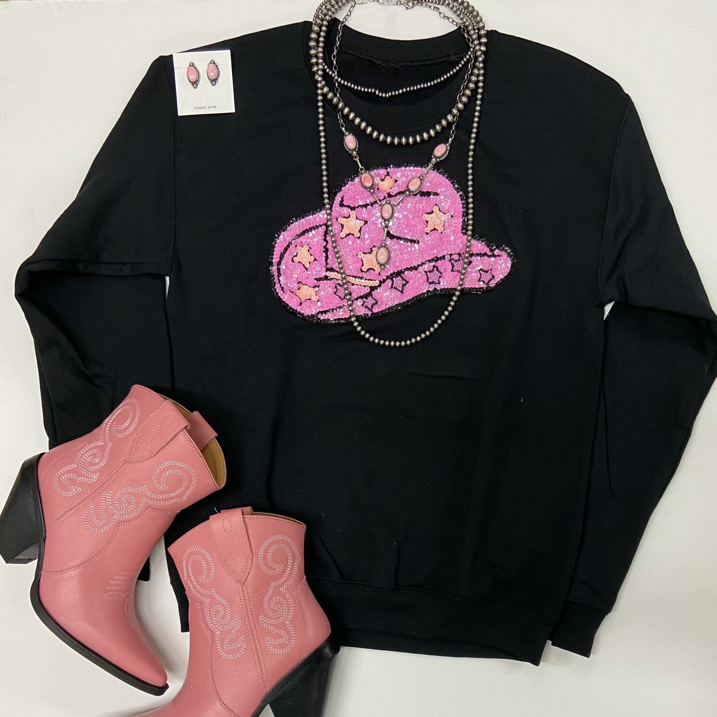A black sweatshirt with a pink sequin patch. It is pictured on a white background with Navajo jewels and pink boots.