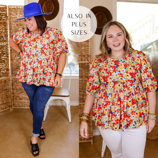 Model is wearing a half sleeve babydoll top with floral patterns in red, yellow, blue and green. Model has this top paired with blue jeans, black heels, gold jewelry, and a blue hat. 
